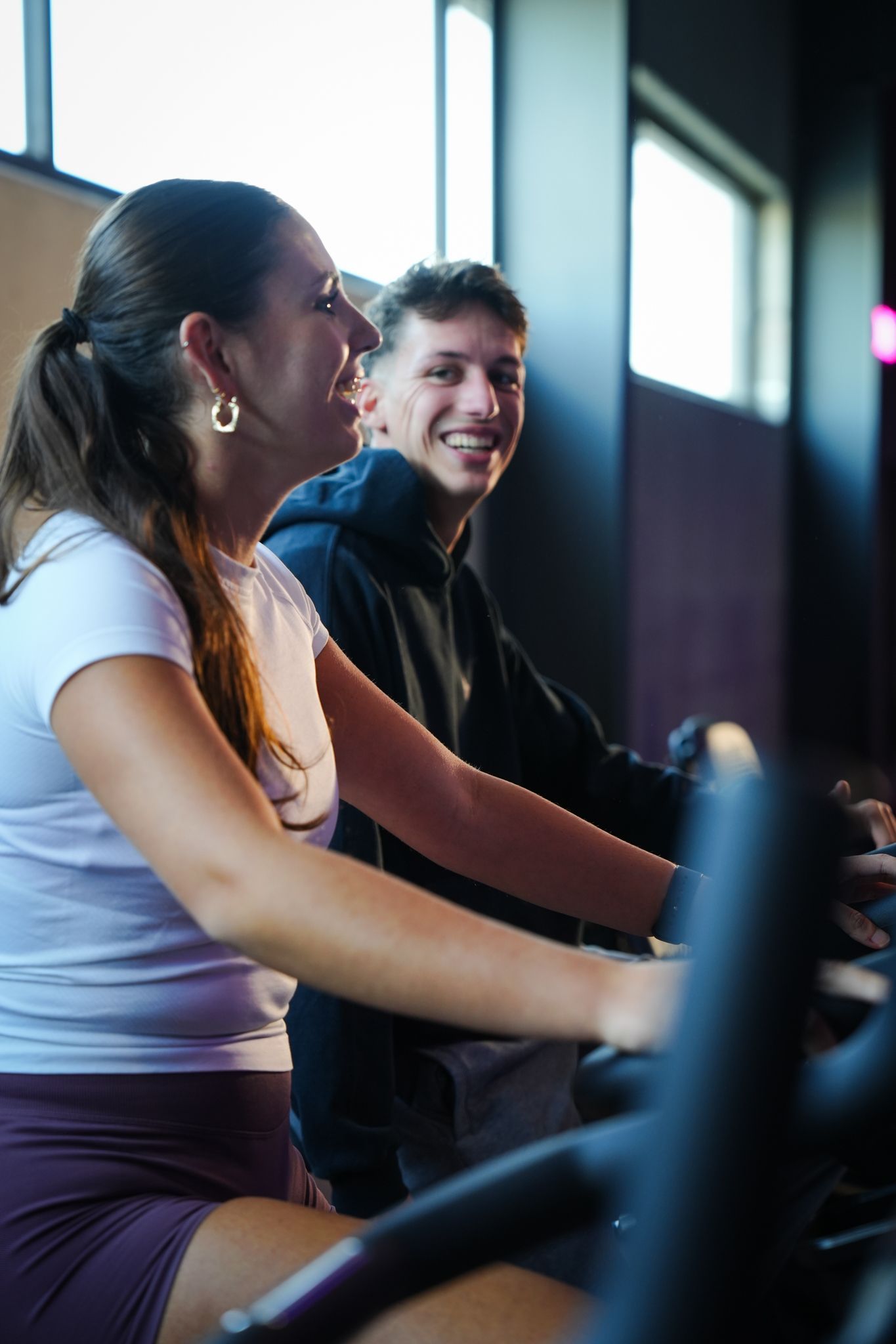 Twee mensen lachend terwijl ze op hometrainers in een sportschool zitten.