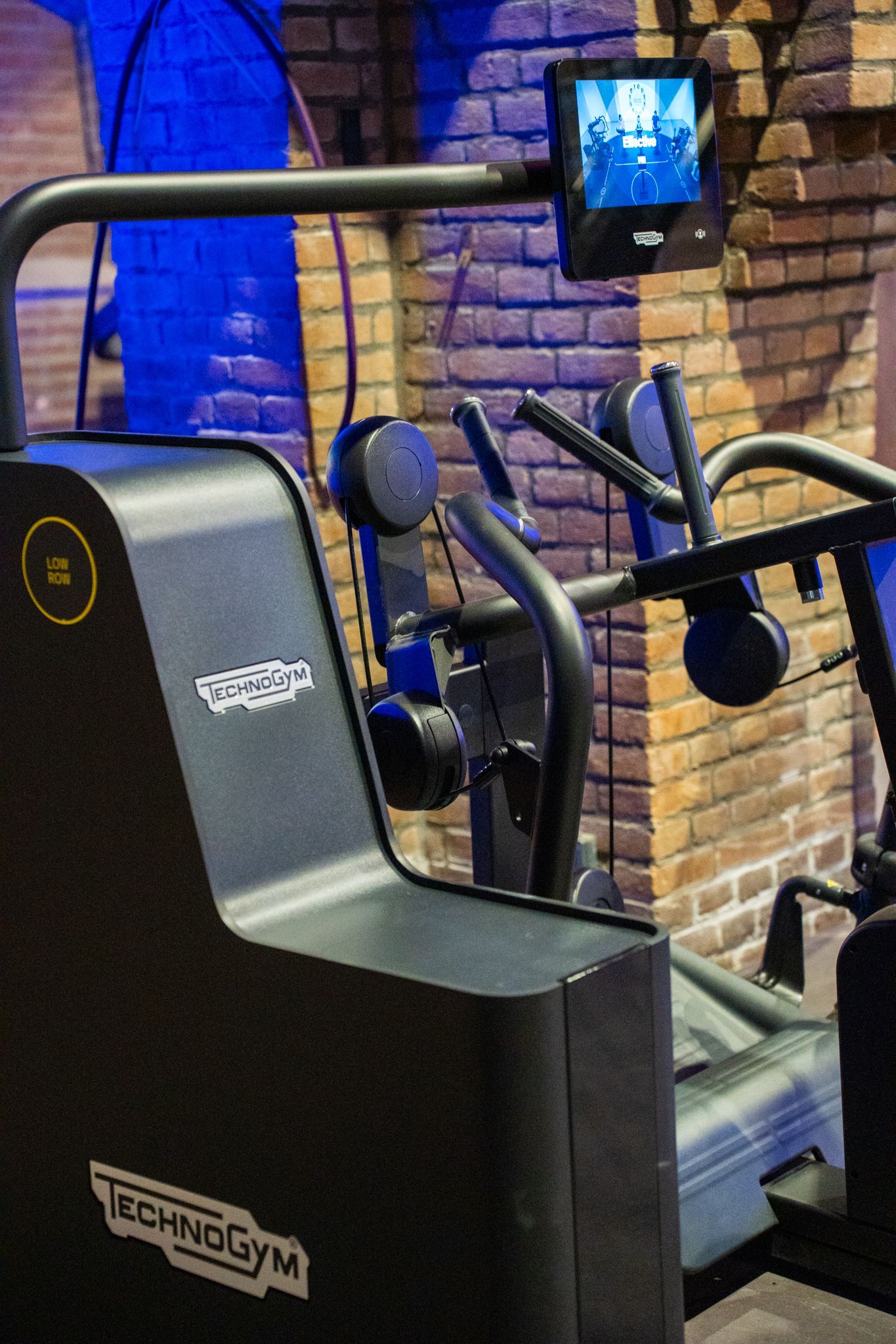 Traploopmachine in een sportschool met een bakstenen muur op de achtergrond en een monitor.