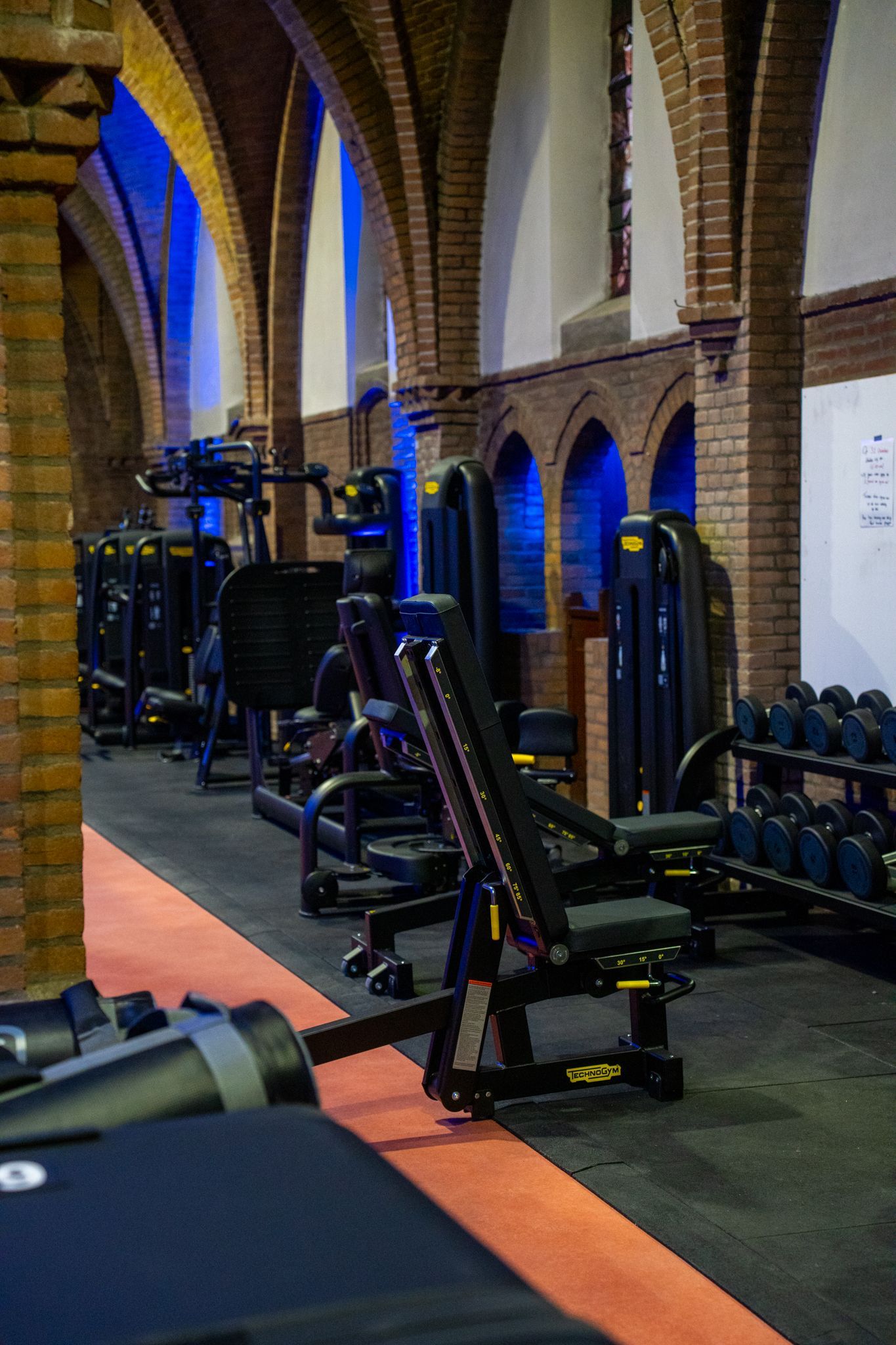 Het interieur van de sportschool heeft gewelfde bakstenen plafonds, fitnessapparaten en een rode atletiekbaan.