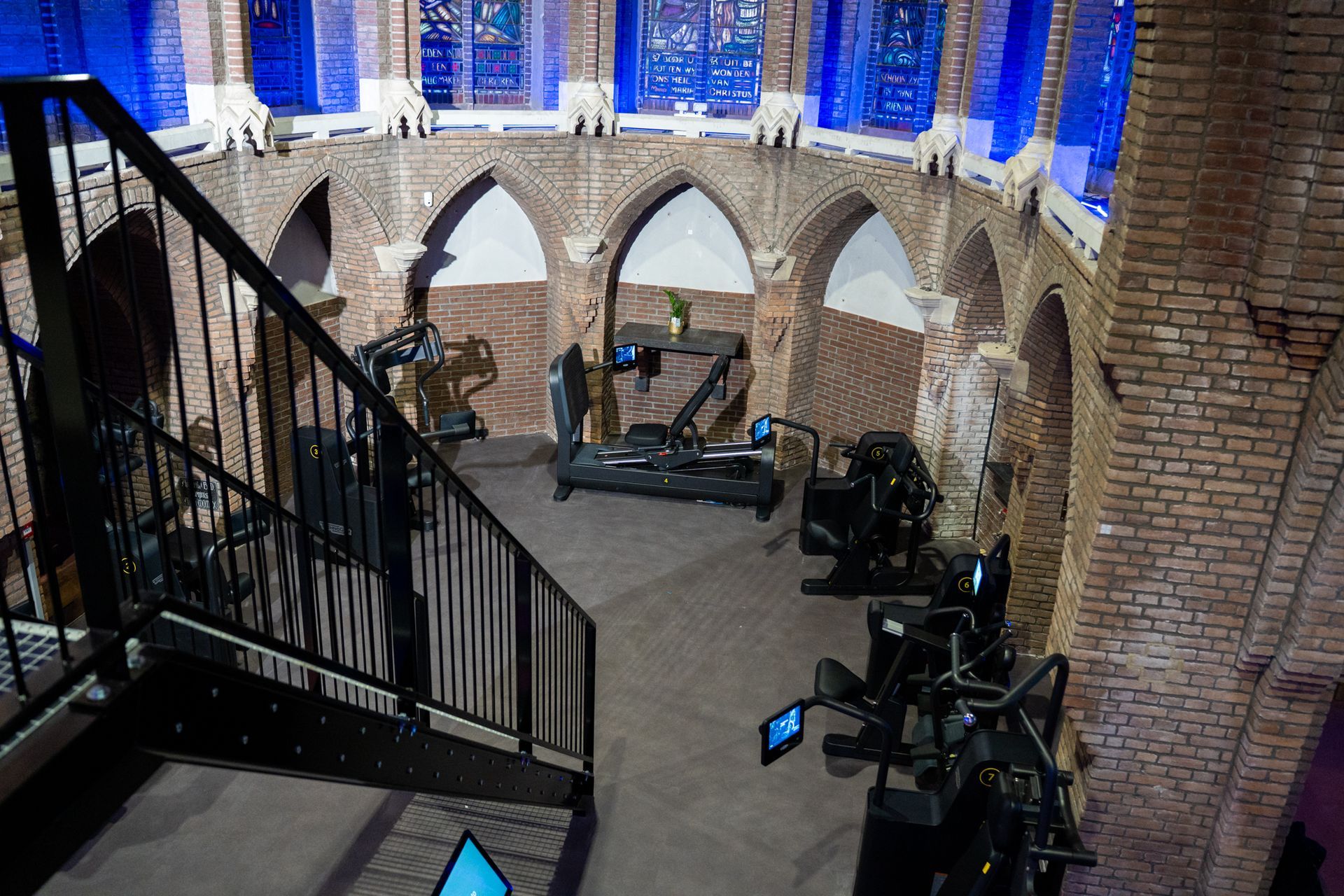 Binnen in een bakstenen gebouw met gewelfde plafonds, een trap met een zwarte leuning en zwarte apparatuur.