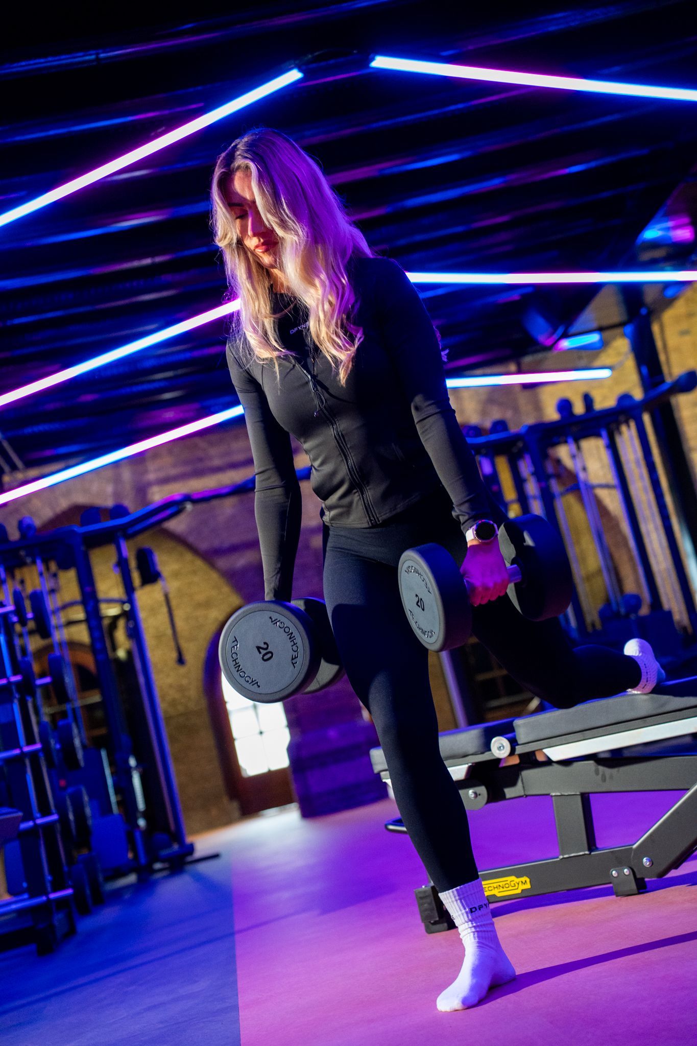 Vrouw in de sportschool met dumbbells, bezig met lunges. Paarse en blauwe verlichting.