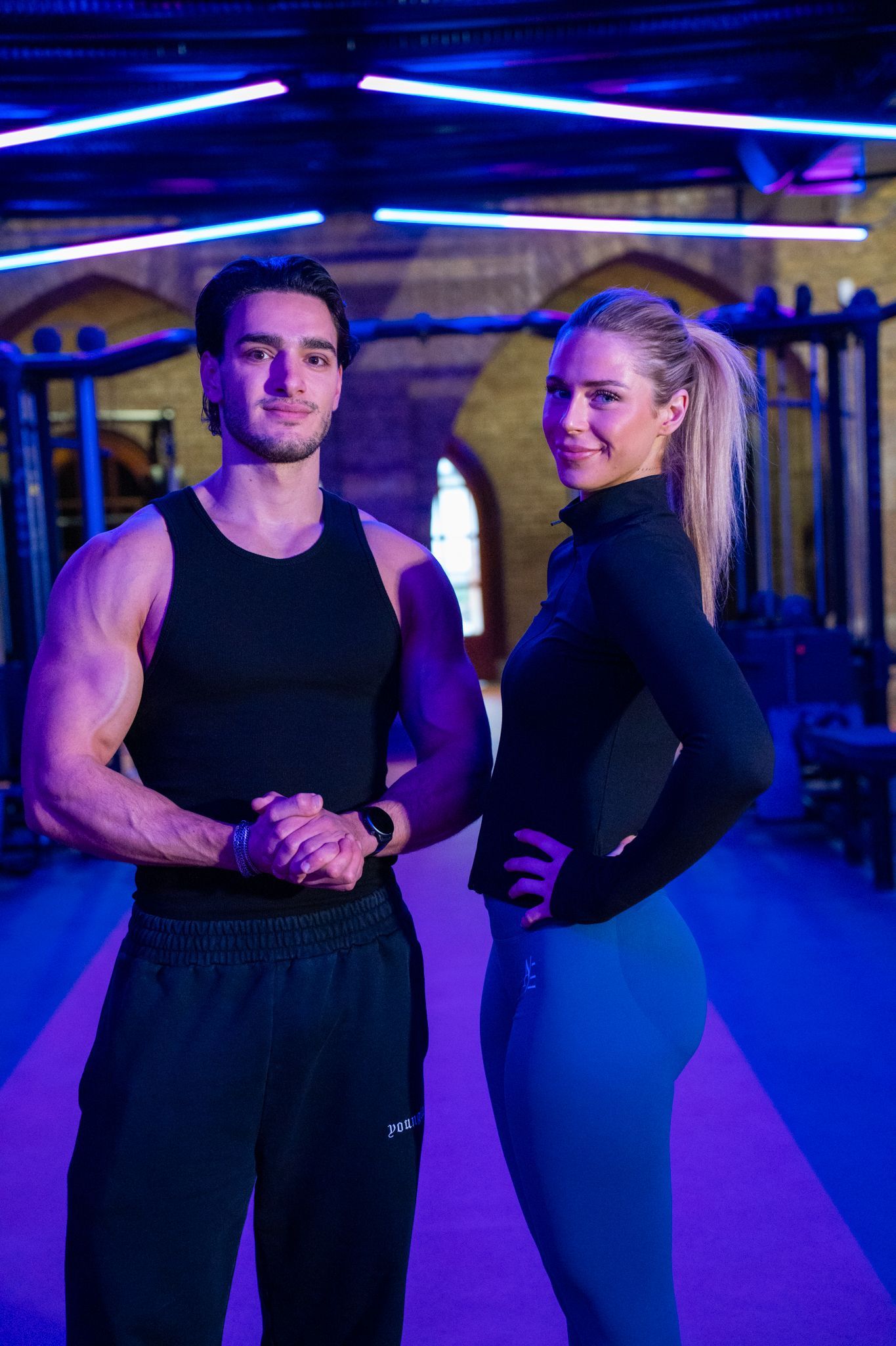 Man en vrouw in de sportschool. Man in een hemdje, vrouw in sportkleding. Blauwe en paarse verlichting.