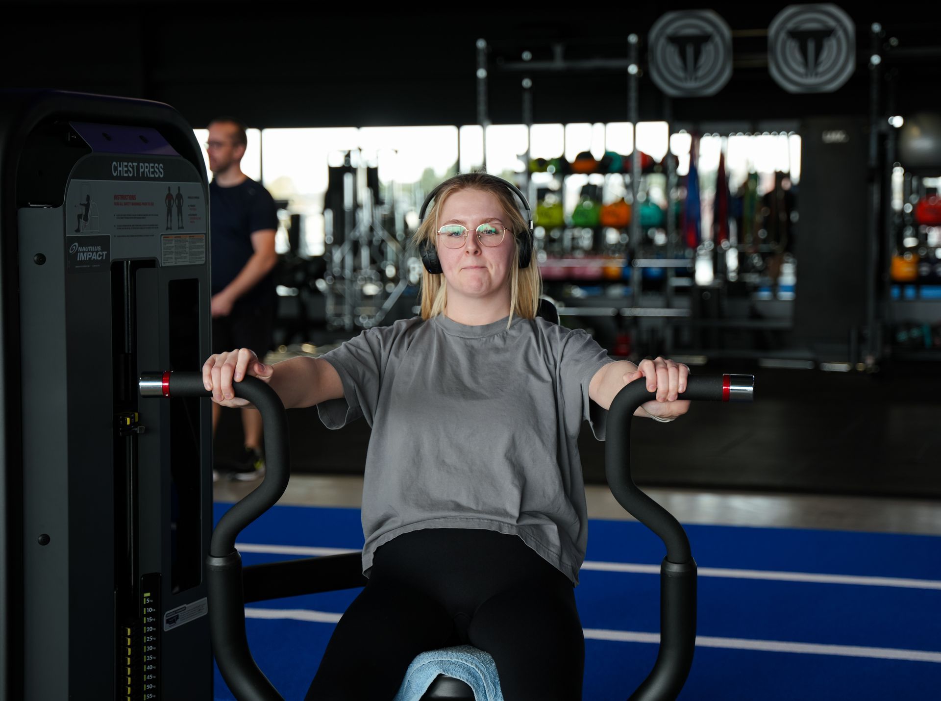 Een vrouw met een koptelefoon fietst op een hometrainer in de sportschool.