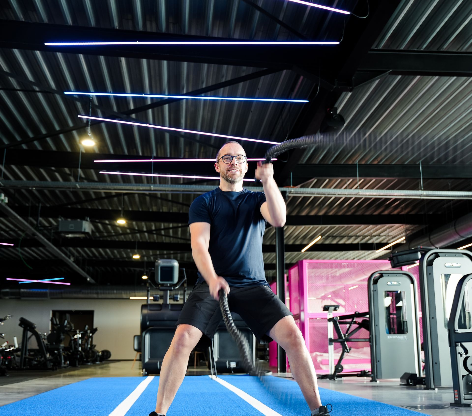 Een man staat op een blauwe mat in een gymzaal en houdt een touw vast.