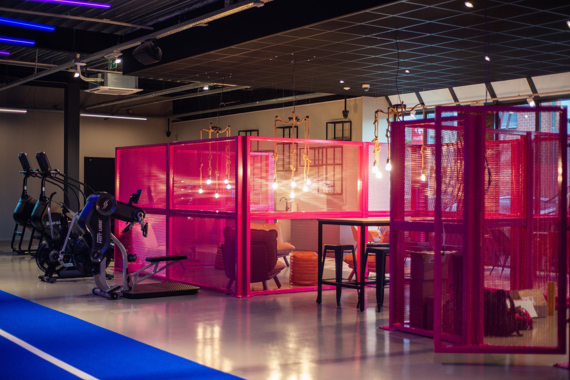 Interieur van de sportschool met roze metalen constructies, hometrainers en een blauwe atletiekbaan.