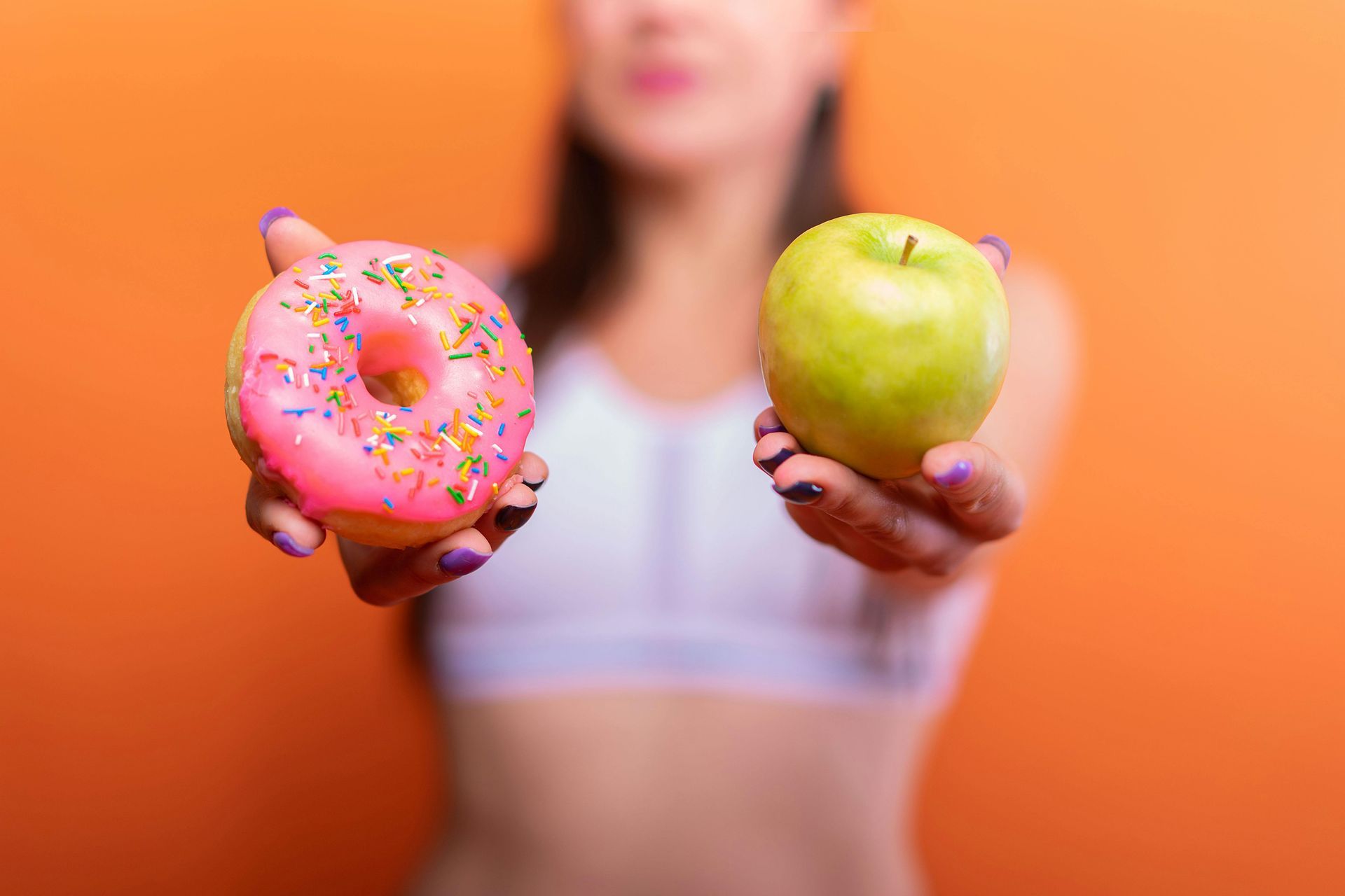 Woman holding a donut and an apple, orange background.