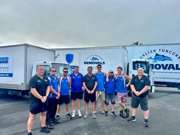 Team of Movers in Blue and Black Uniforms Stand in Front of Trucks — Forster Tuncurry Removals & Storage in Forster, NSW