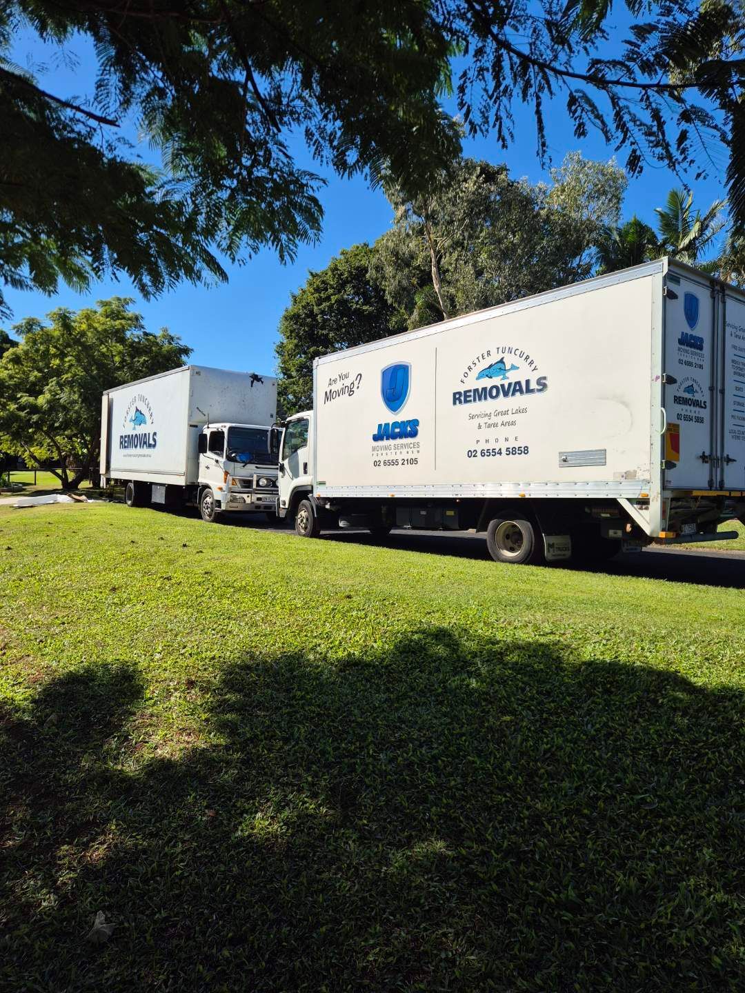 A Row of Moving Trucks Are Parked in a Grassy Field — Forster Tuncurry Removals & Storage in Tuncurry, NSW