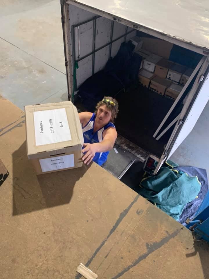 A Man is Holding a Cardboard Box in Front of a Trailer — Forster Tuncurry Removals & Storage in Tuncurry, NSW