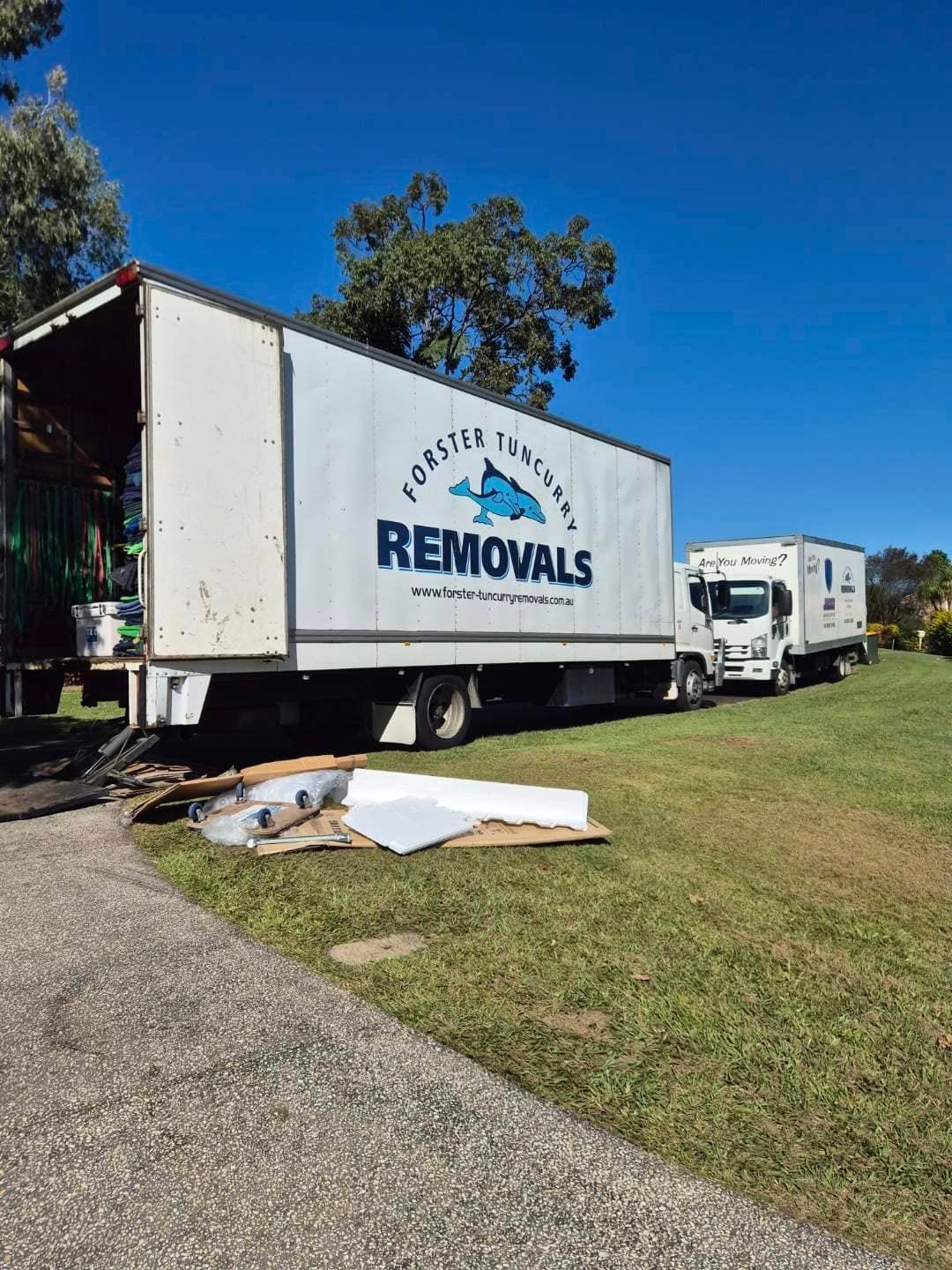 Two Moving Trucks Are Parked Next to Each Other in a Grassy Field — Forster Tuncurry Removals & Storage in Tuncurry, NSW