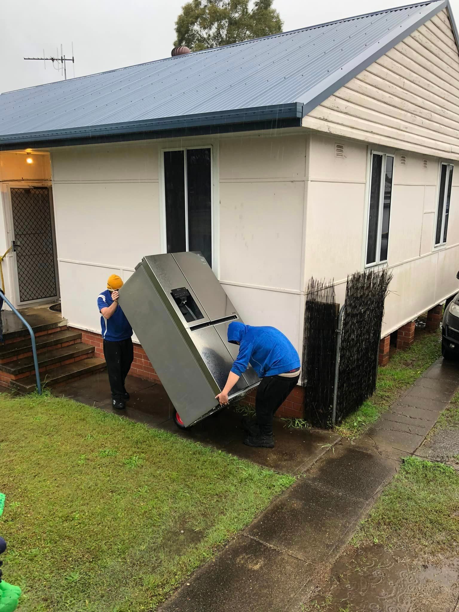 Two Men Are Carrying a Refrigerator Into a House — Forster Tuncurry Removals & Storage in Tuncurry, NSW