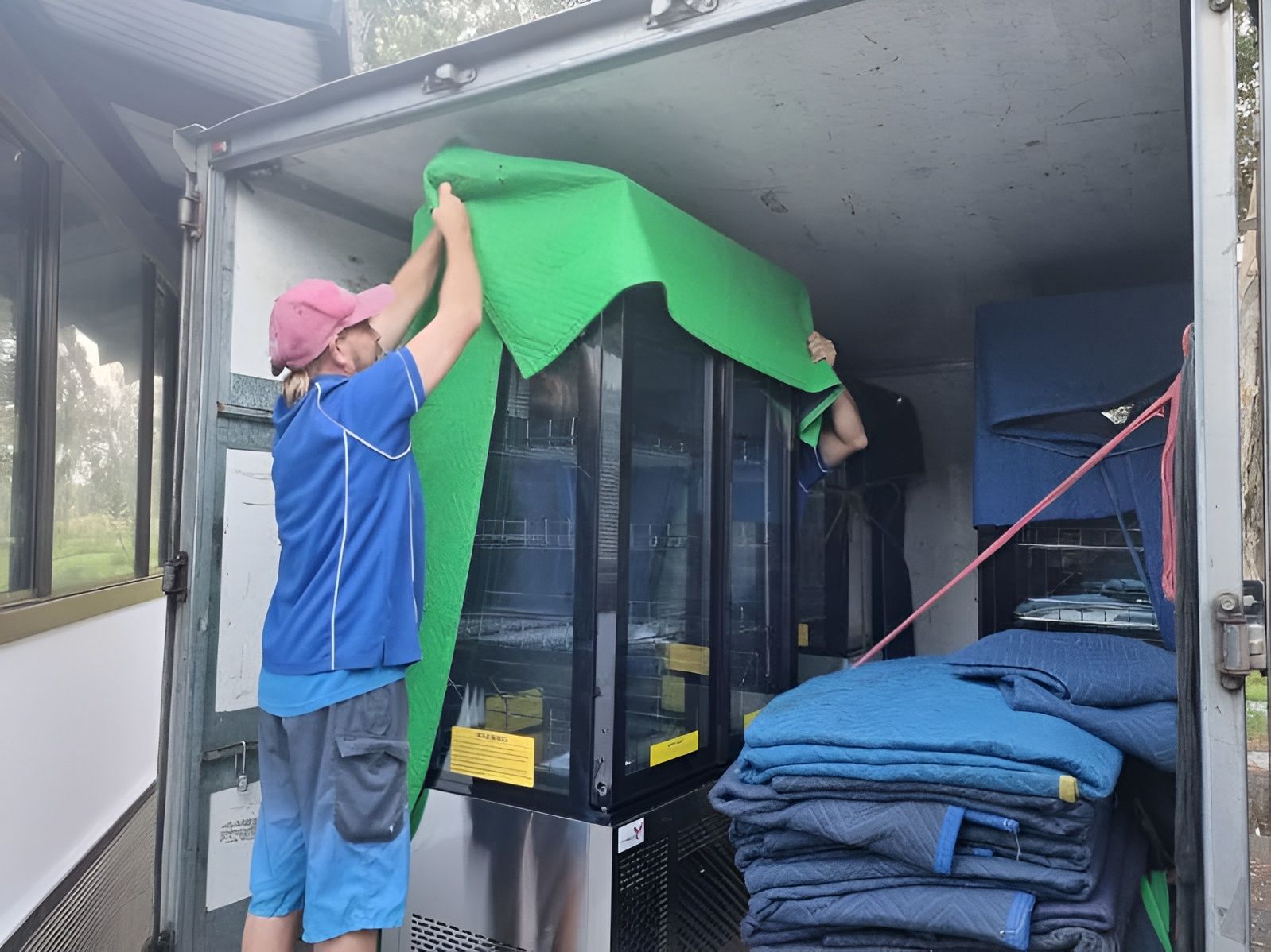 A Man is Holding a Green Cloth Over a Refrigerator in a Truck — Forster Tuncurry Removals & Storage in Tuncurry, NSW