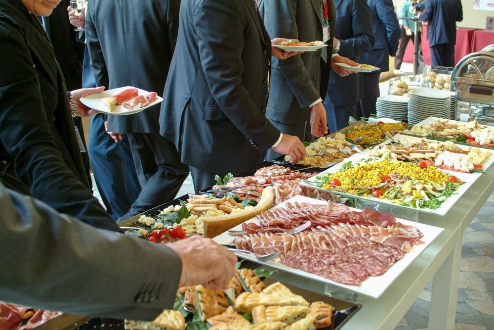 A group of corporate people are standing around a table with plates of food.