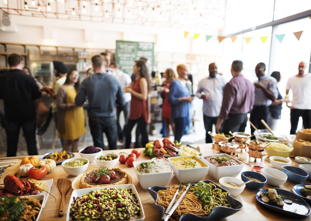 A group of people are standing around a table full of food.