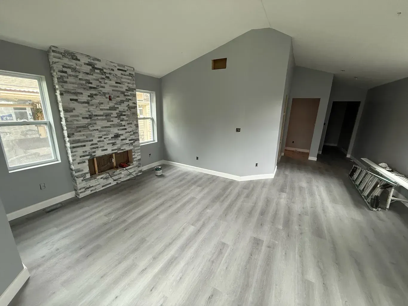 Empty living room with gray walls, wood-look flooring, brick fireplace, and two windows.