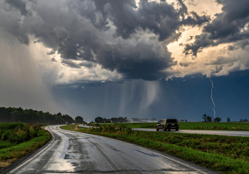 Rural road under severe storm clouds with heavy rain and lightning.