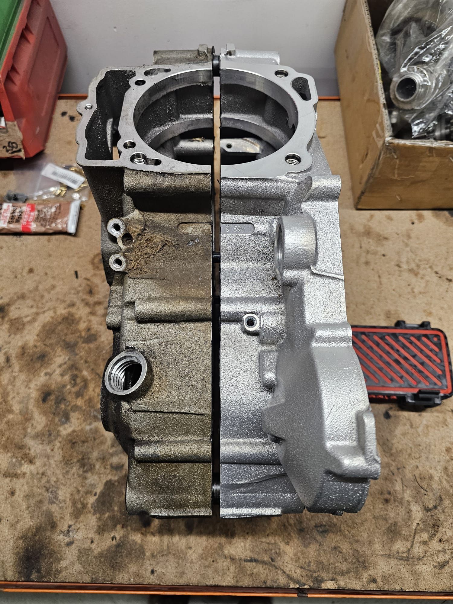 Half-cleaned motorcycle engine casing showing before/after. Darker, dirty left side; clean, silver-painted right side.