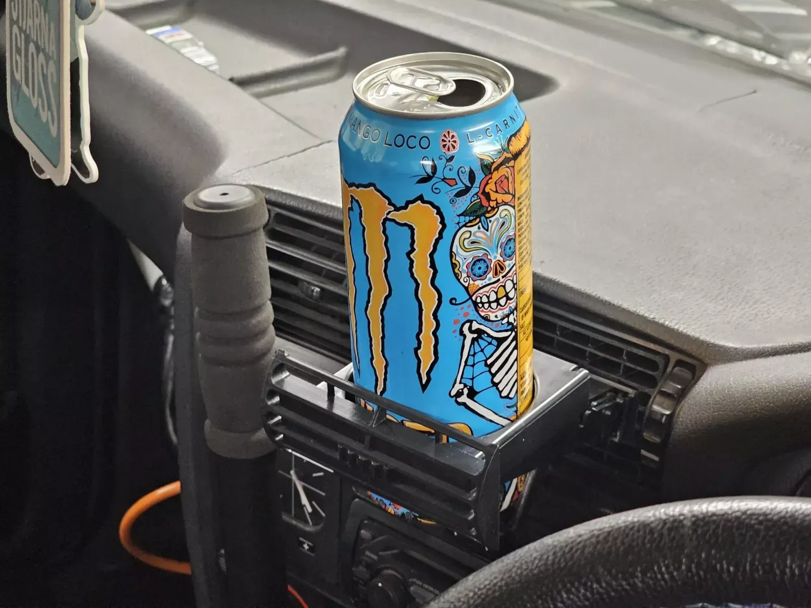 A can of Monster energy drink sits in a car's cup holder, next to the gear shift.