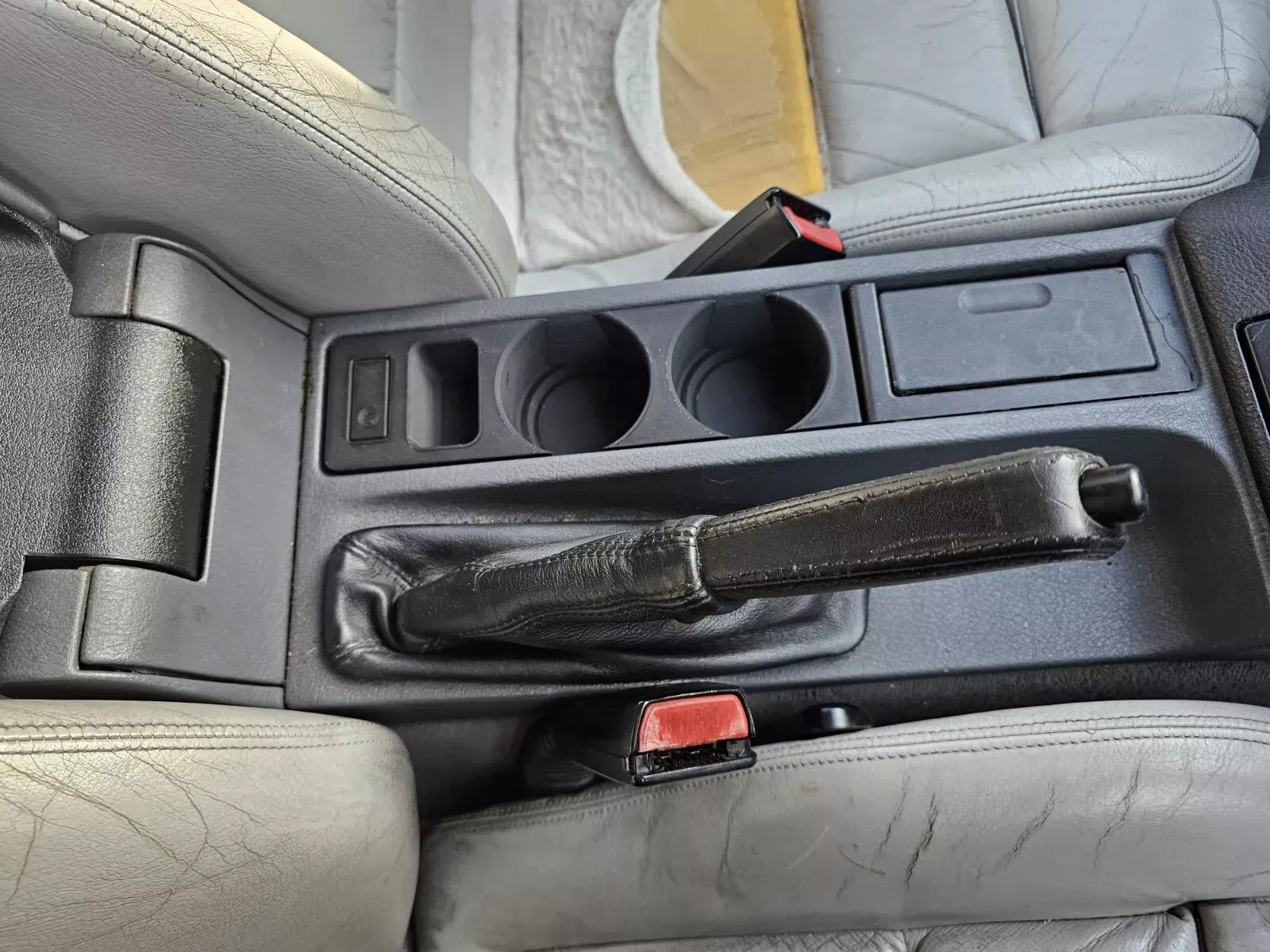 Interior car console with cup holders, emergency brake, and seat belt buckles. Gray seats.