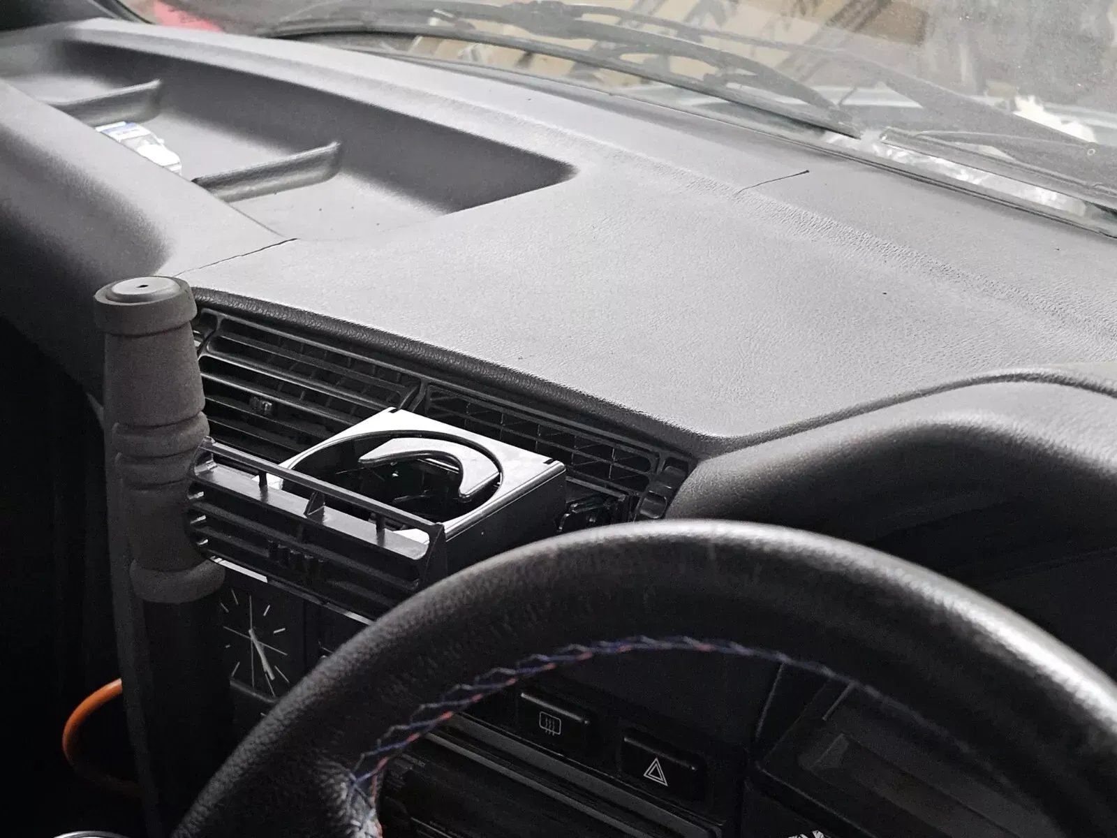 Black car dashboard, steering wheel in foreground. Glove box, vents, and gear shift visible.