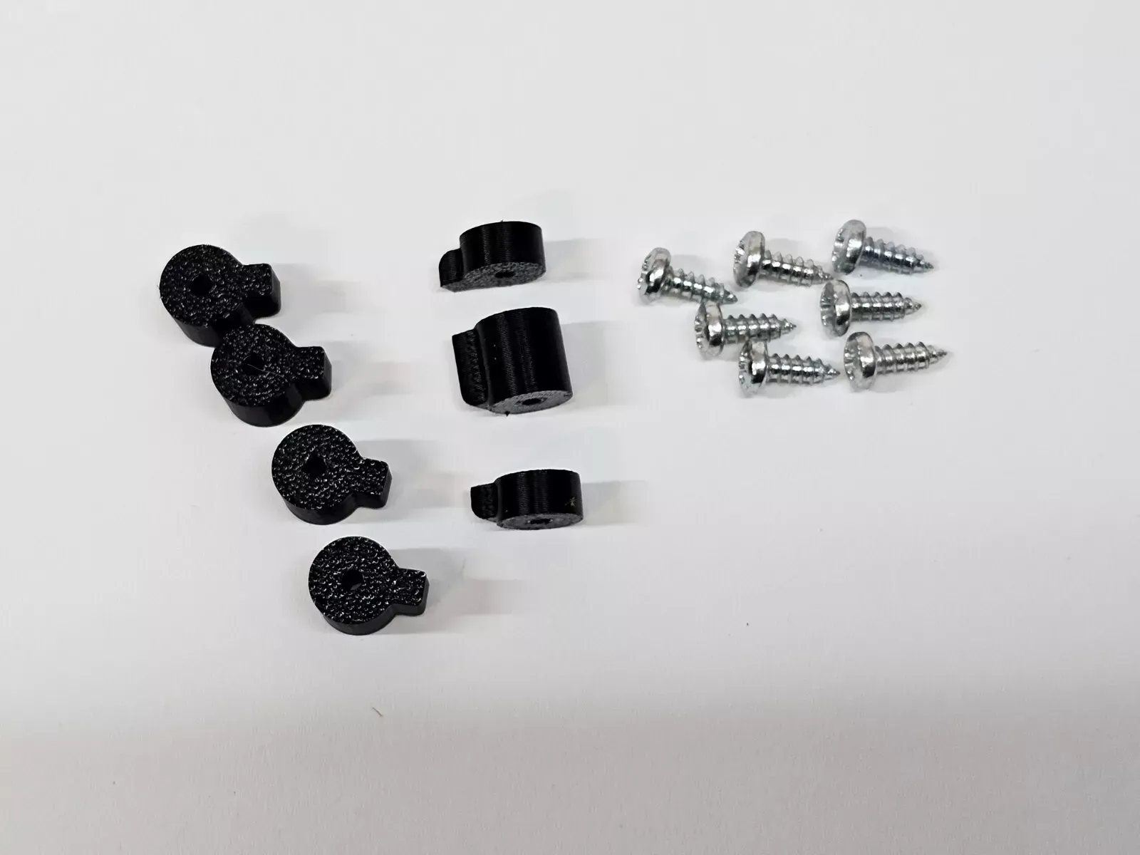 Black plastic parts and silver screws on white surface.