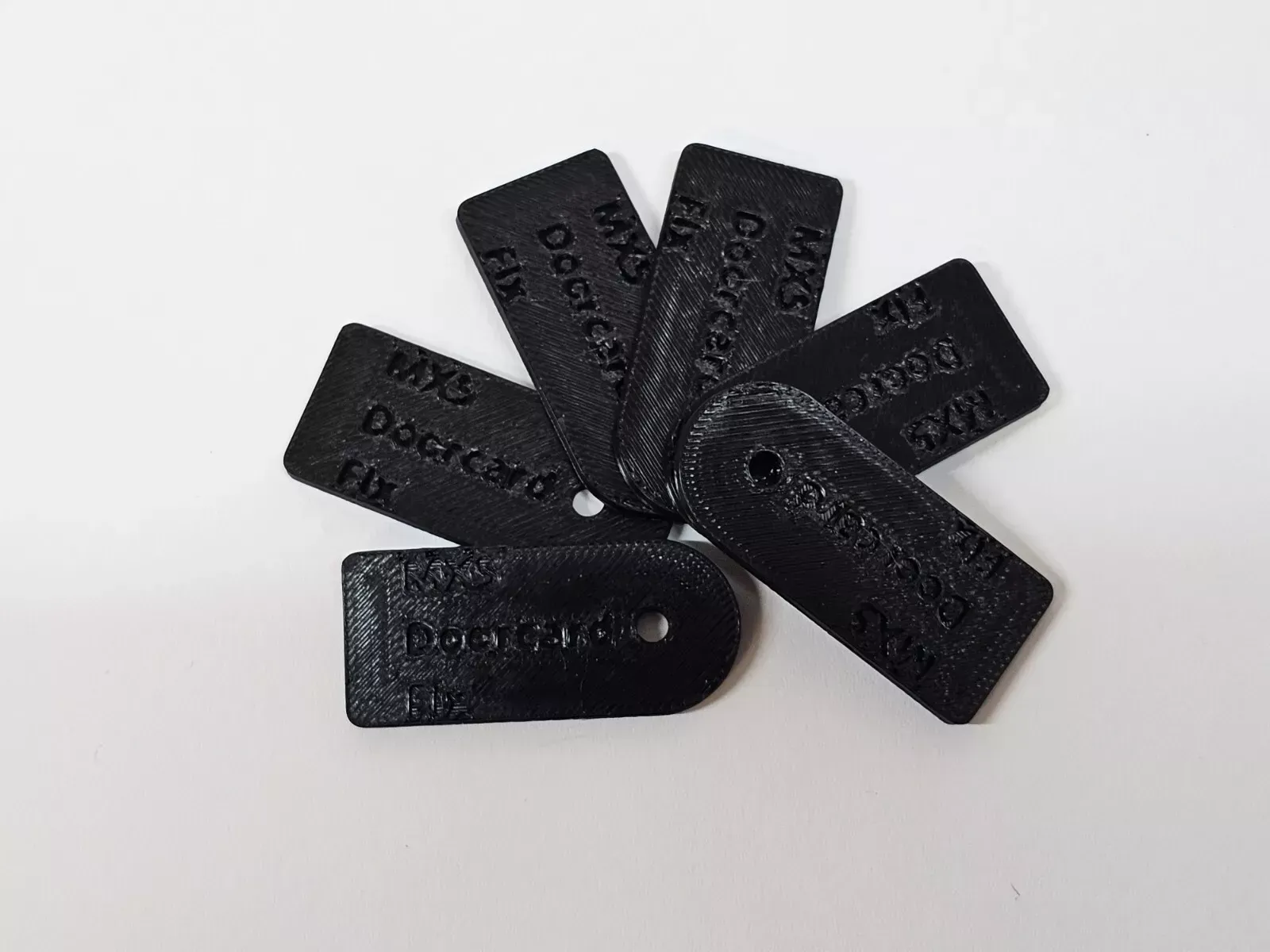 Black 3D-printed tags with text, fanned out on a white surface. They likely label or identify items.