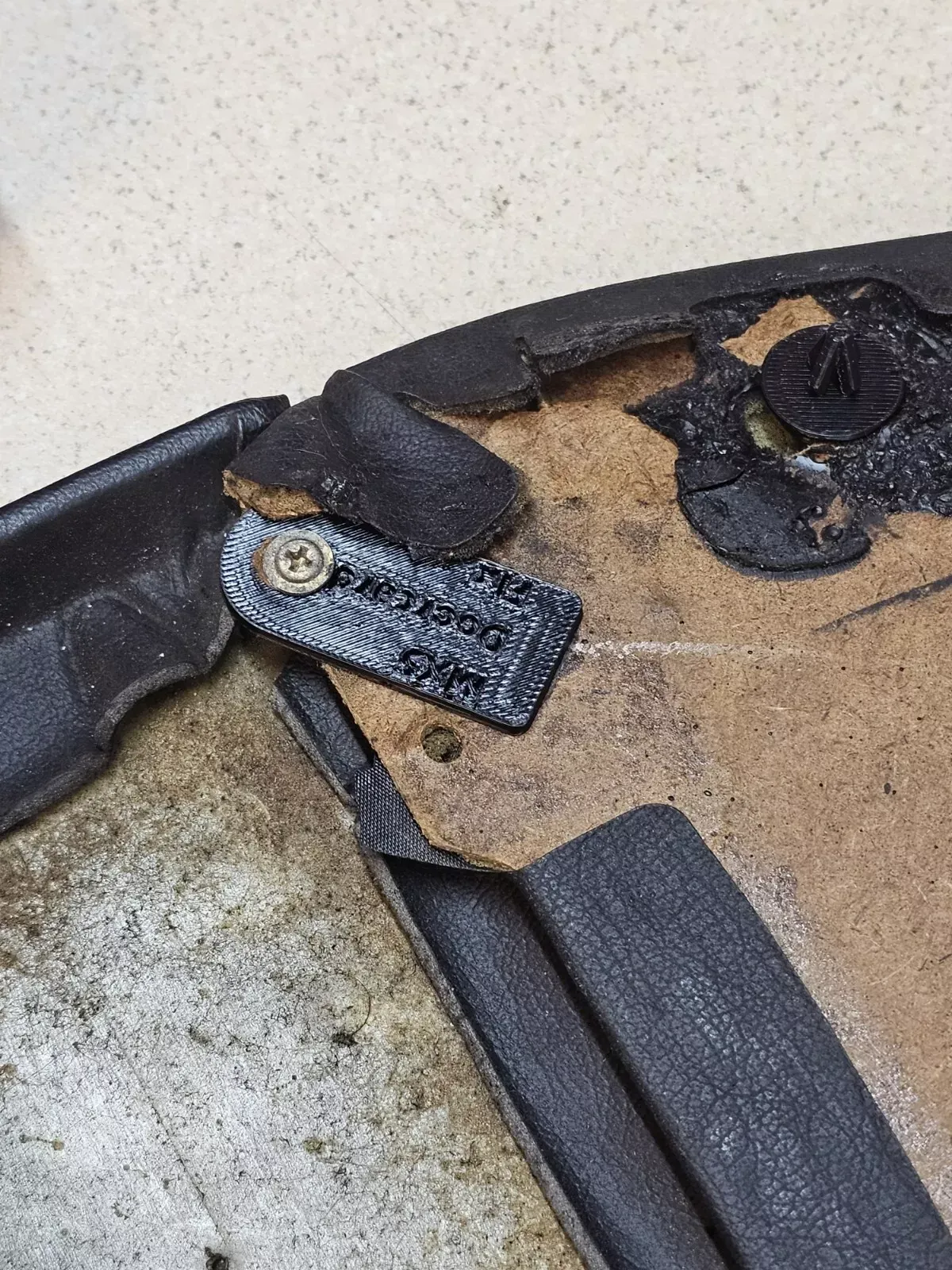 Close-up shows a torn black interior panel with a small tag screwed in. The tag reads