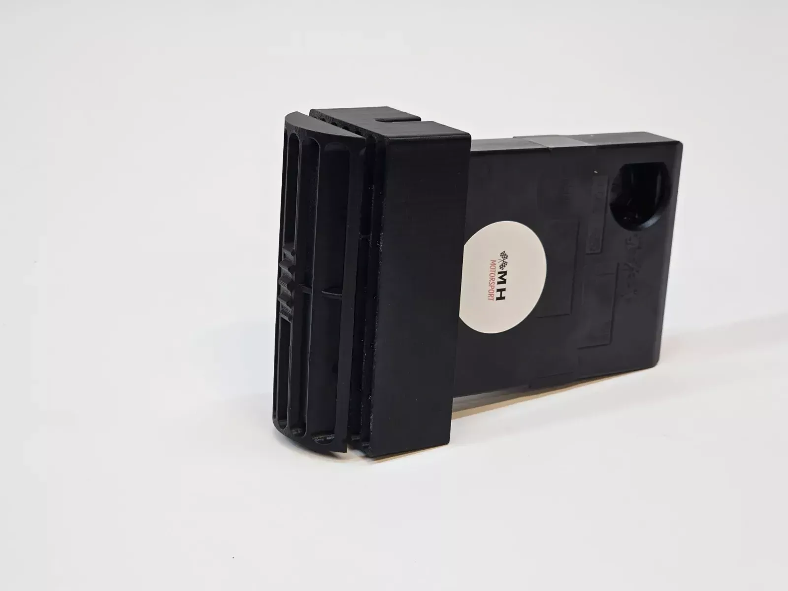 Black rectangular device with vents and a circular label, on a white surface.