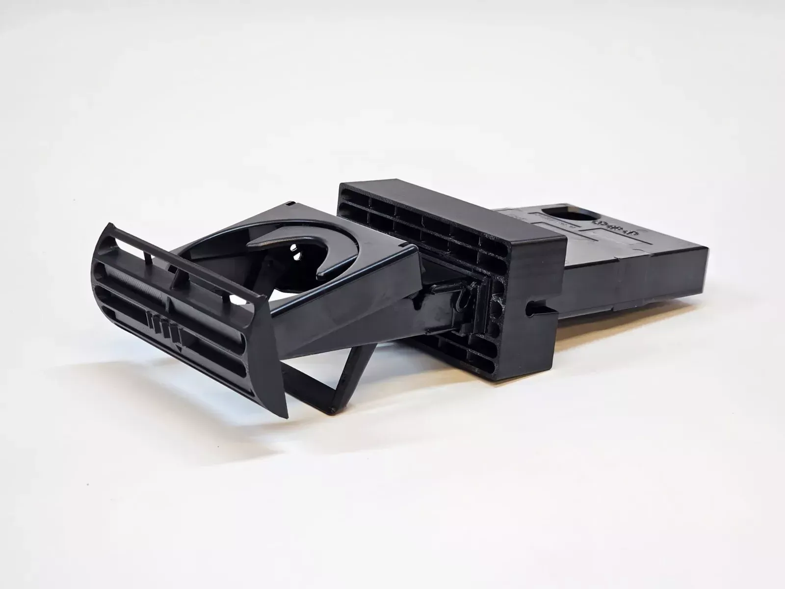 Black plastic car cup holder, attached to a vent, on a white surface.