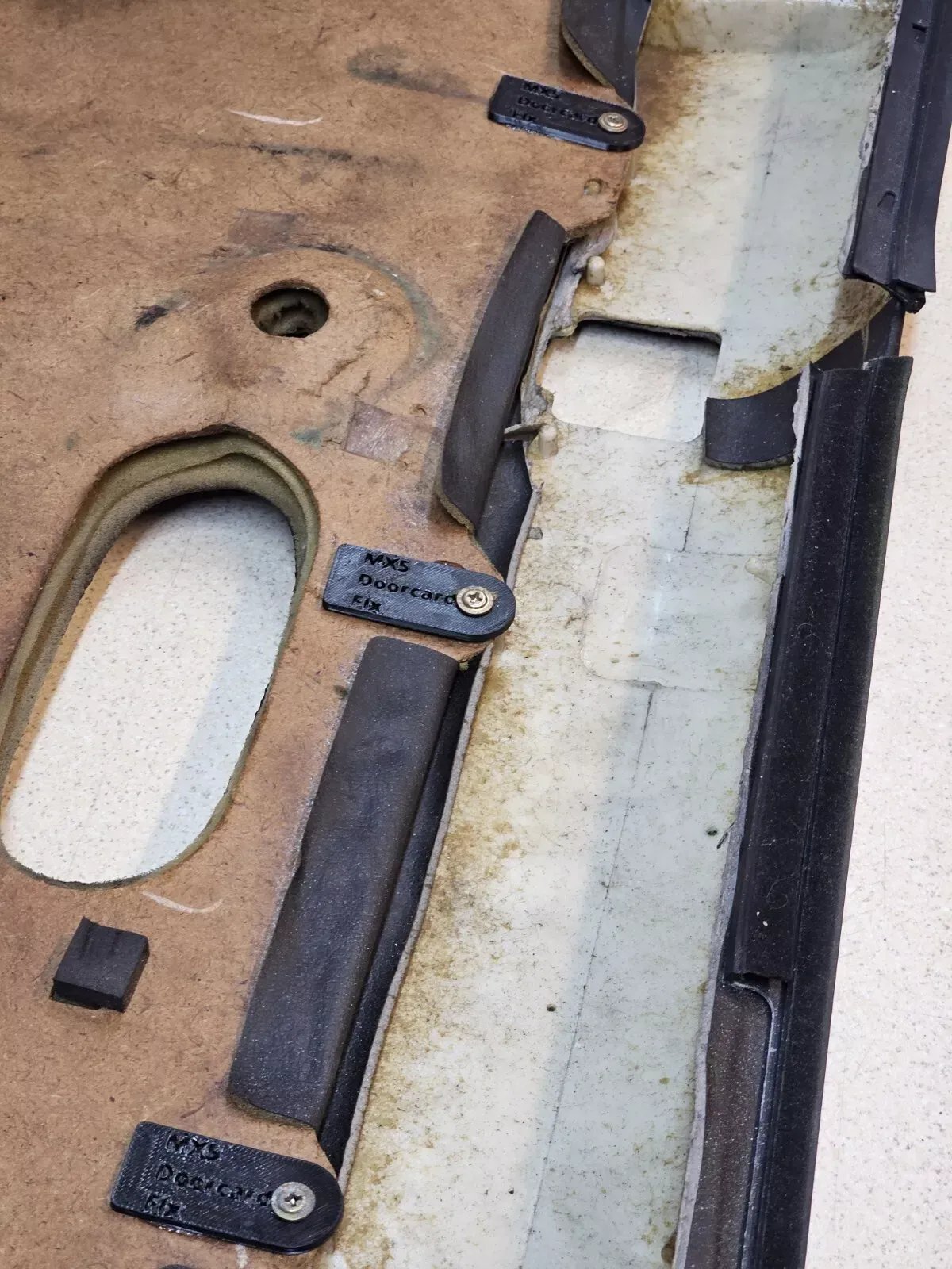 Close-up of a worn car door panel with black rubber trim, showing mounting points and fabric.