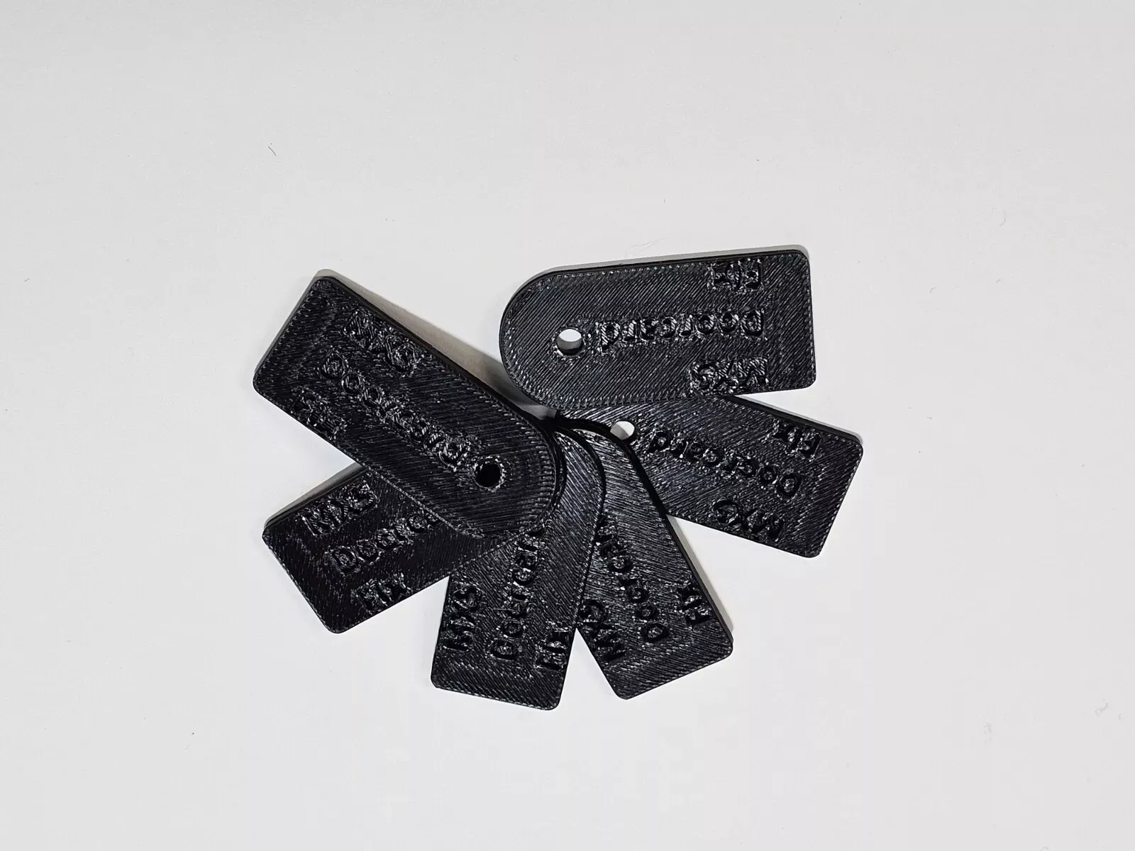 Black rectangular 3D-printed tags with rounded ends and holes, arranged on a white surface.