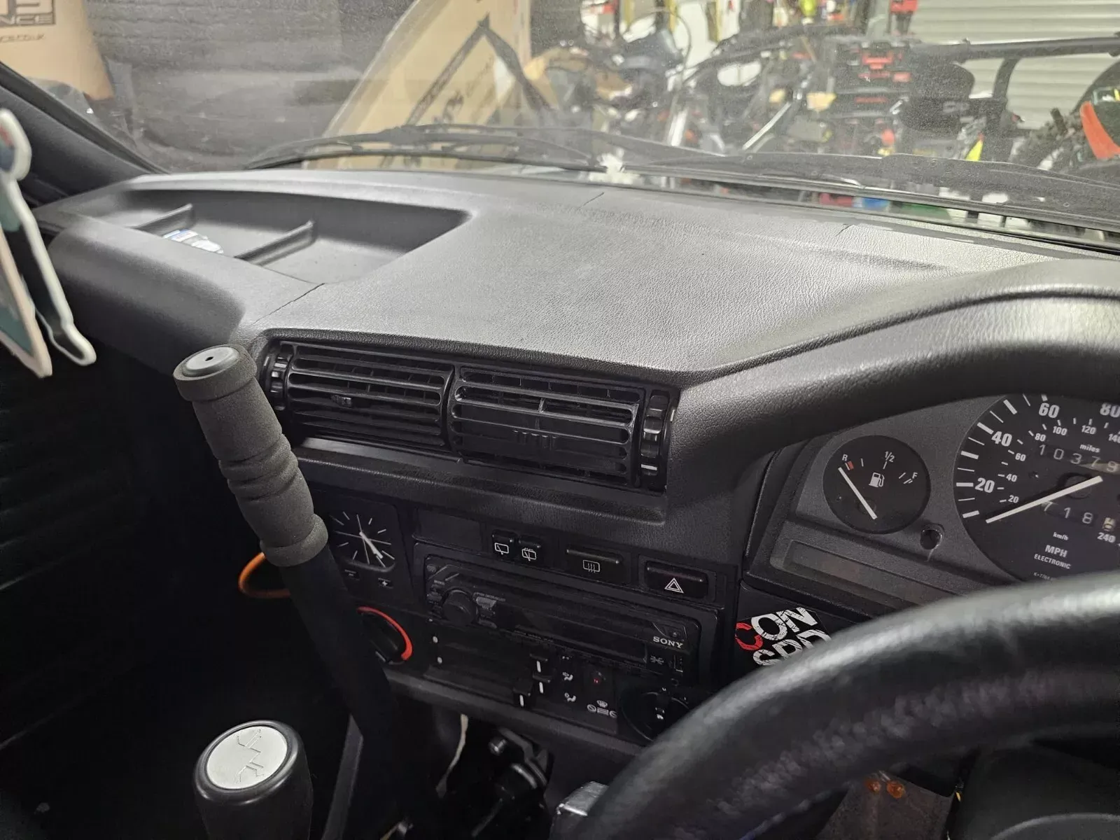 A Monster energy drink can in a custom-built car cup holder on a car dashboard.