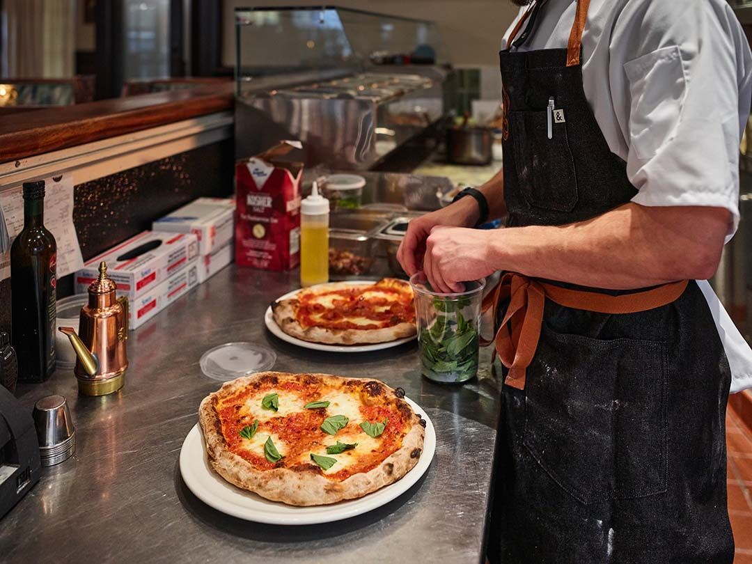 A man in an apron is preparing a pizza in a kitchen.