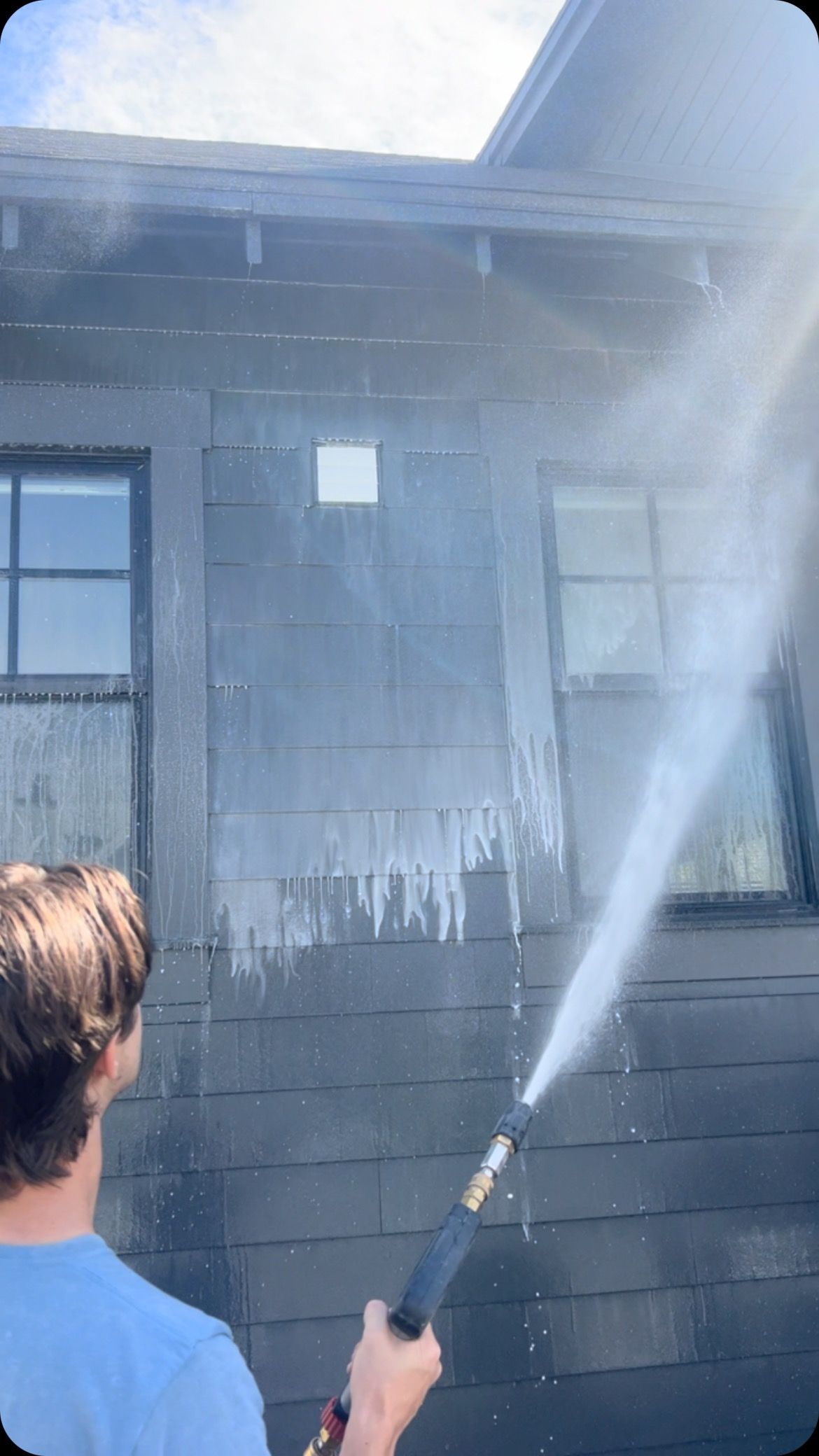 A man is using a high pressure washer to clean the side of a house.