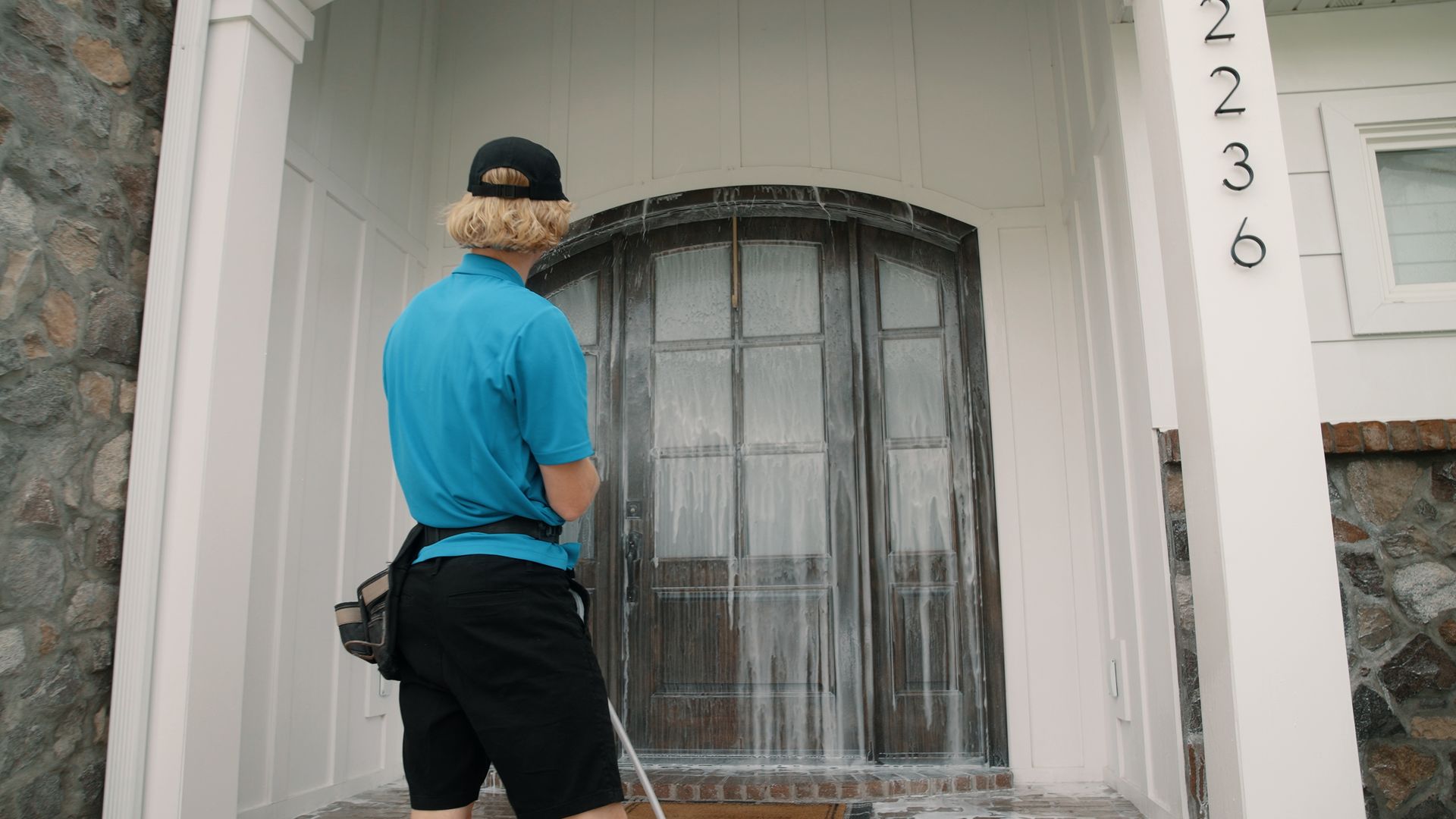 A man is cleaning the front door of a house with a pressure washer.