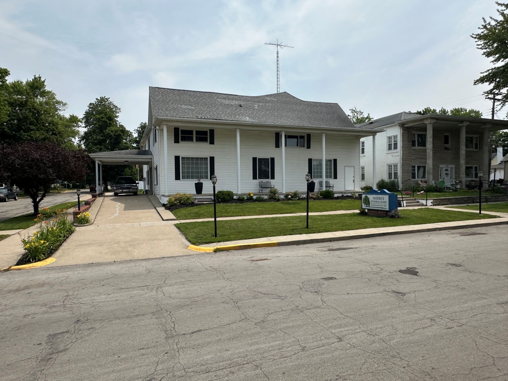 A large white house with a gray roof is sitting on the corner of a street.