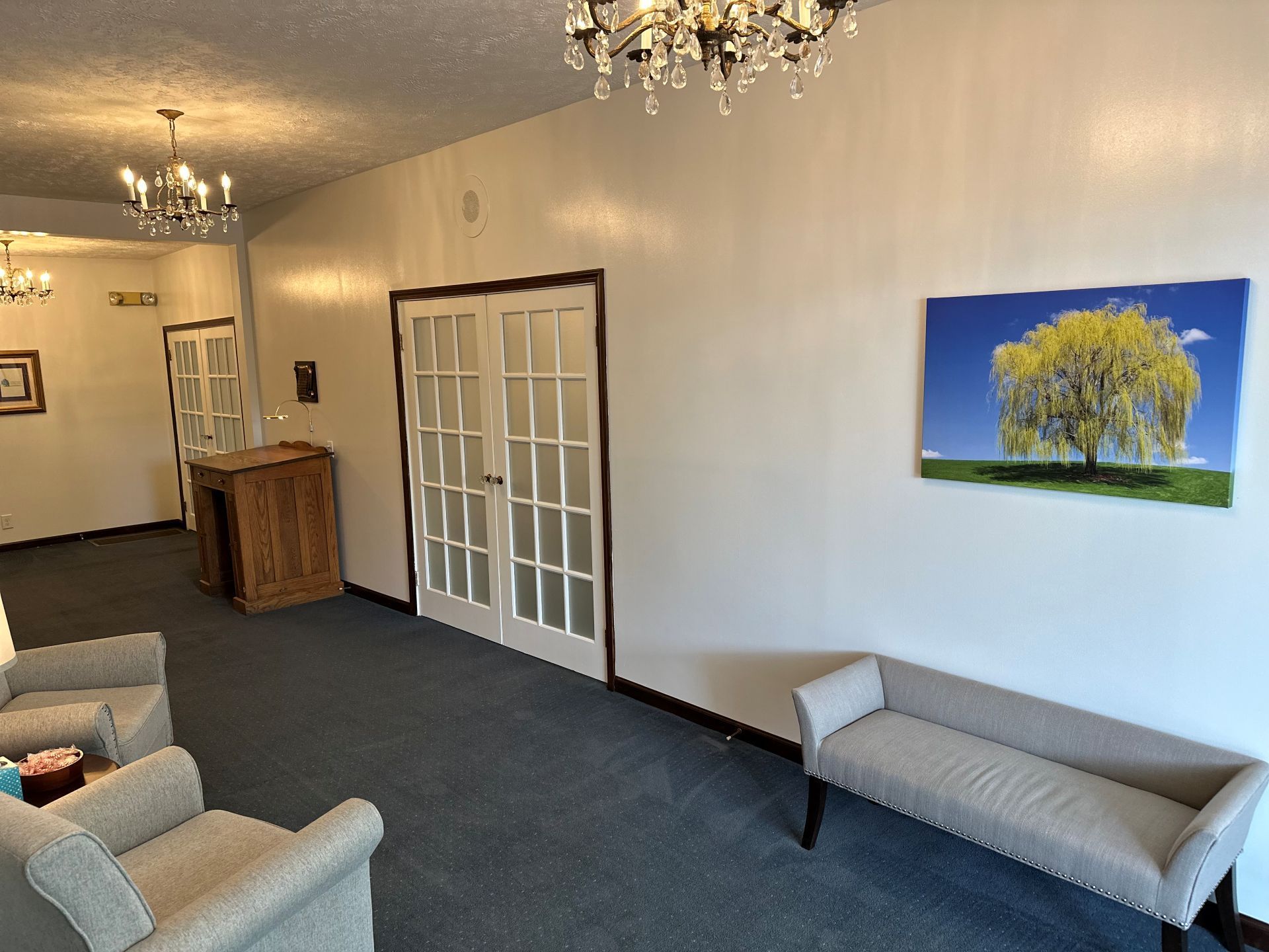 A living room with chairs , a bench and a painting of a tree on the wall.