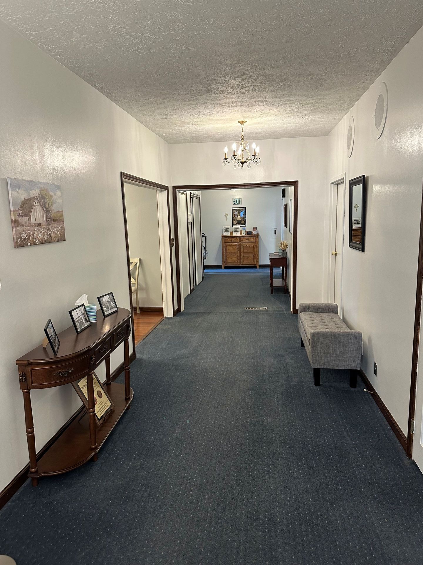 A long hallway with blue carpet and white walls leading to a room.
