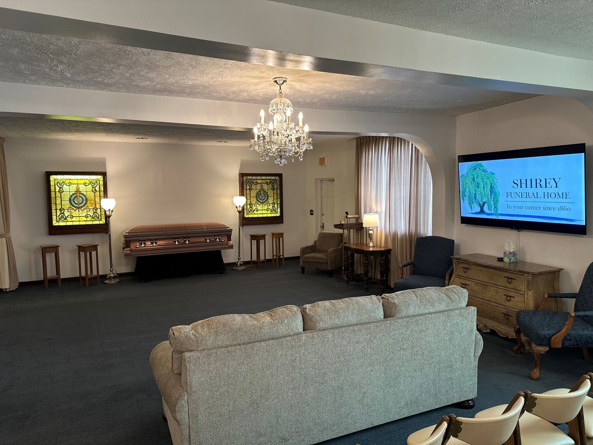 A living room with a couch , chairs , a television and a chandelier.
