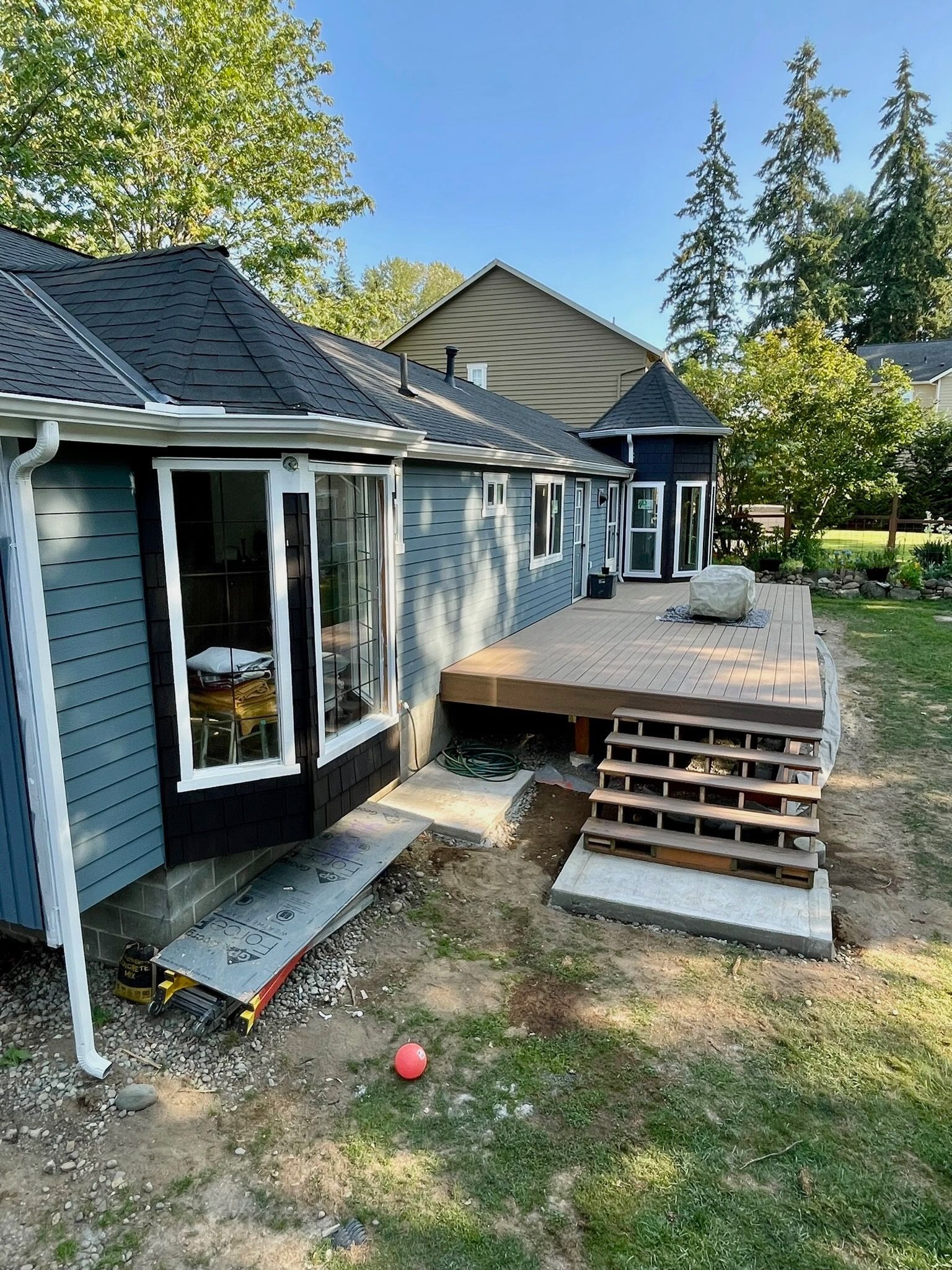A blue house with a new back deck and unfinished staircase, viewed from a grassy yard on a sunny day.