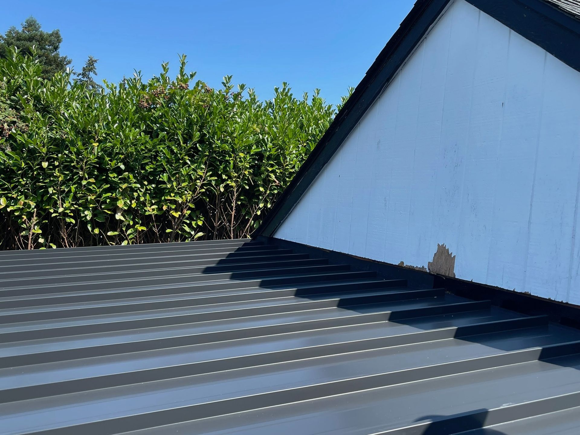 A dark, ribbed metal roof meets a white wooden gable wall with a small patch of peeling paint near the roofline.