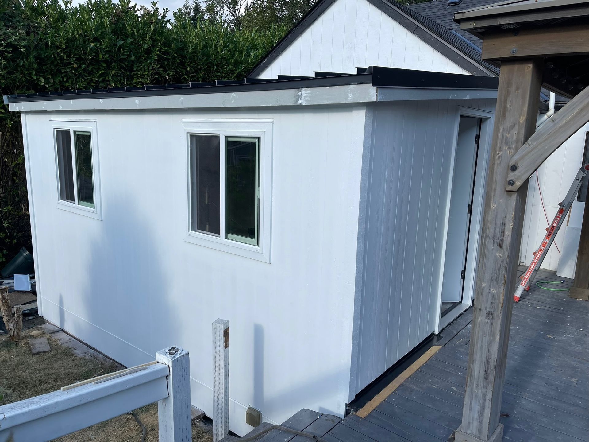 A small, dark blue shed with a white-trimmed door and windows, standing in a backyard on a concrete patio.
