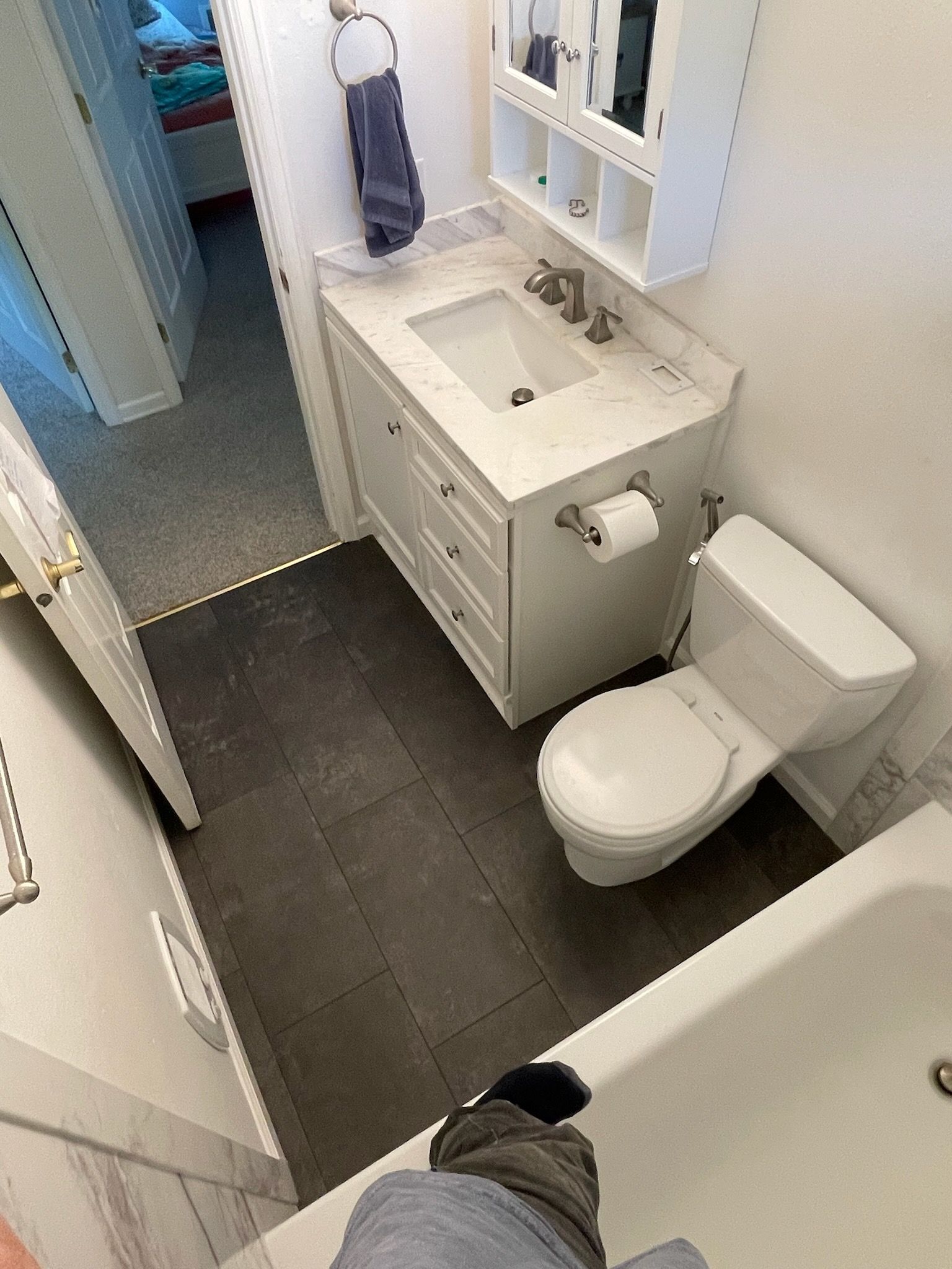 High-angle view of a bathroom featuring dark floor tiles, a white vanity cabinet with a sink, and a white toilet.