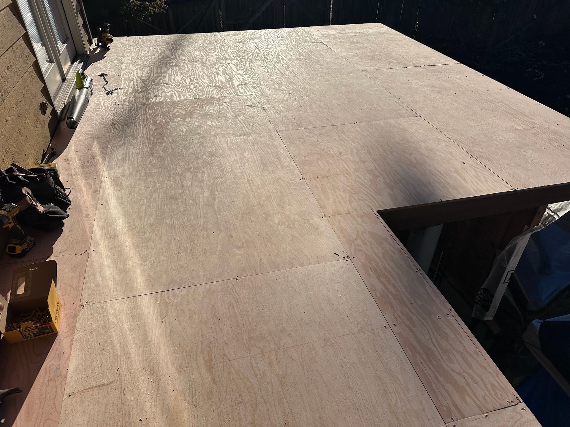 A newly installed plywood subfloor on an outdoor deck frame next to the side of a building.