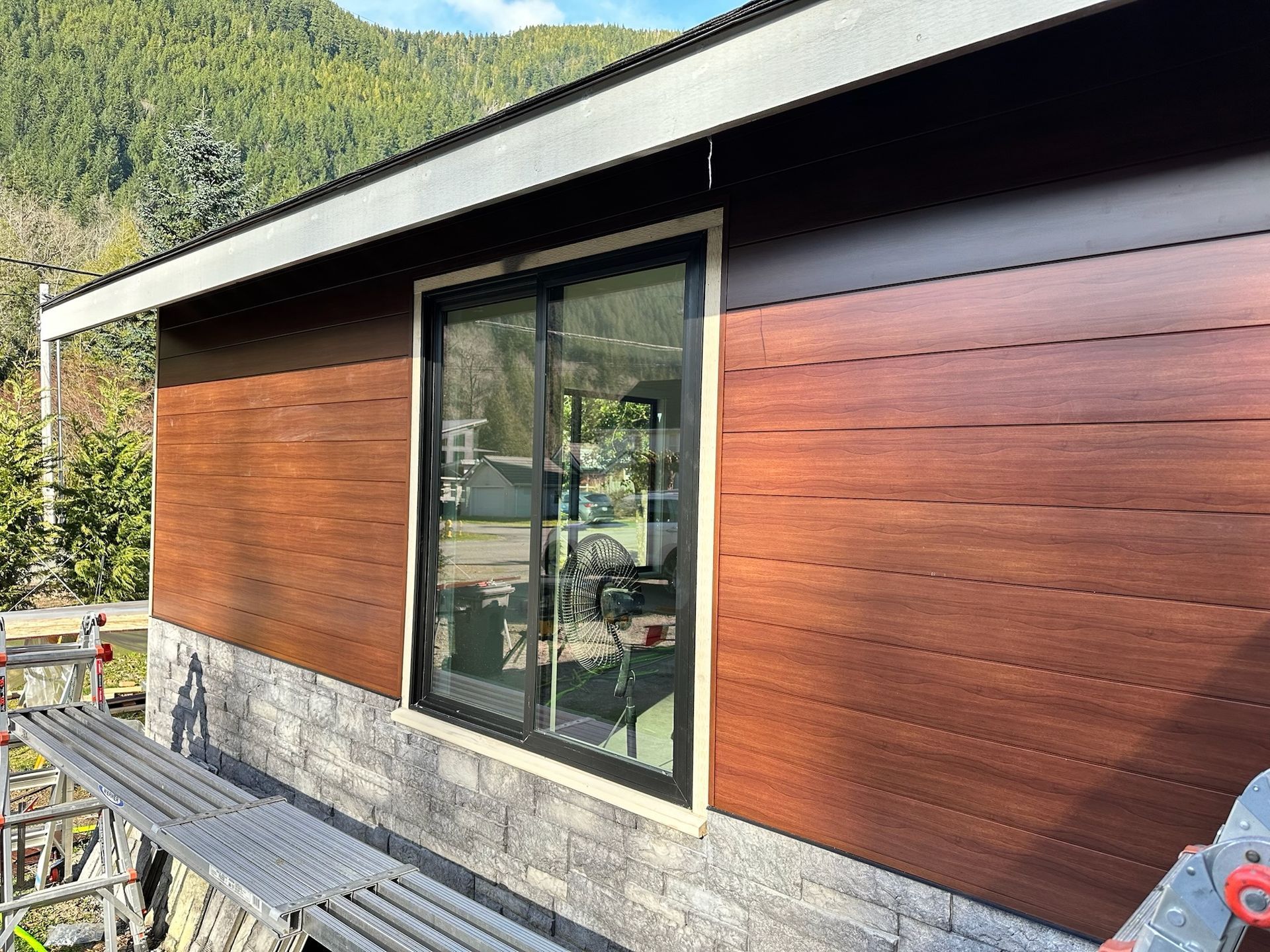 A blue house with a dark roof and a multi-sided bay window, featuring a wooden deck in a grassy backyard.
