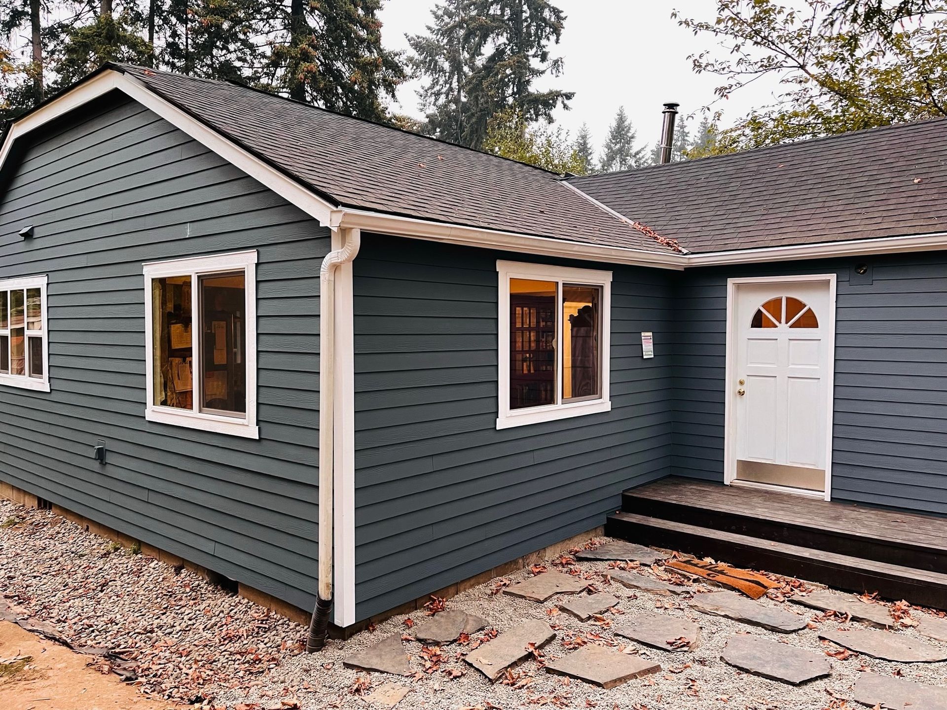 Dark blue, single-story house with white trim, a white front door, steps, and a stone patio.