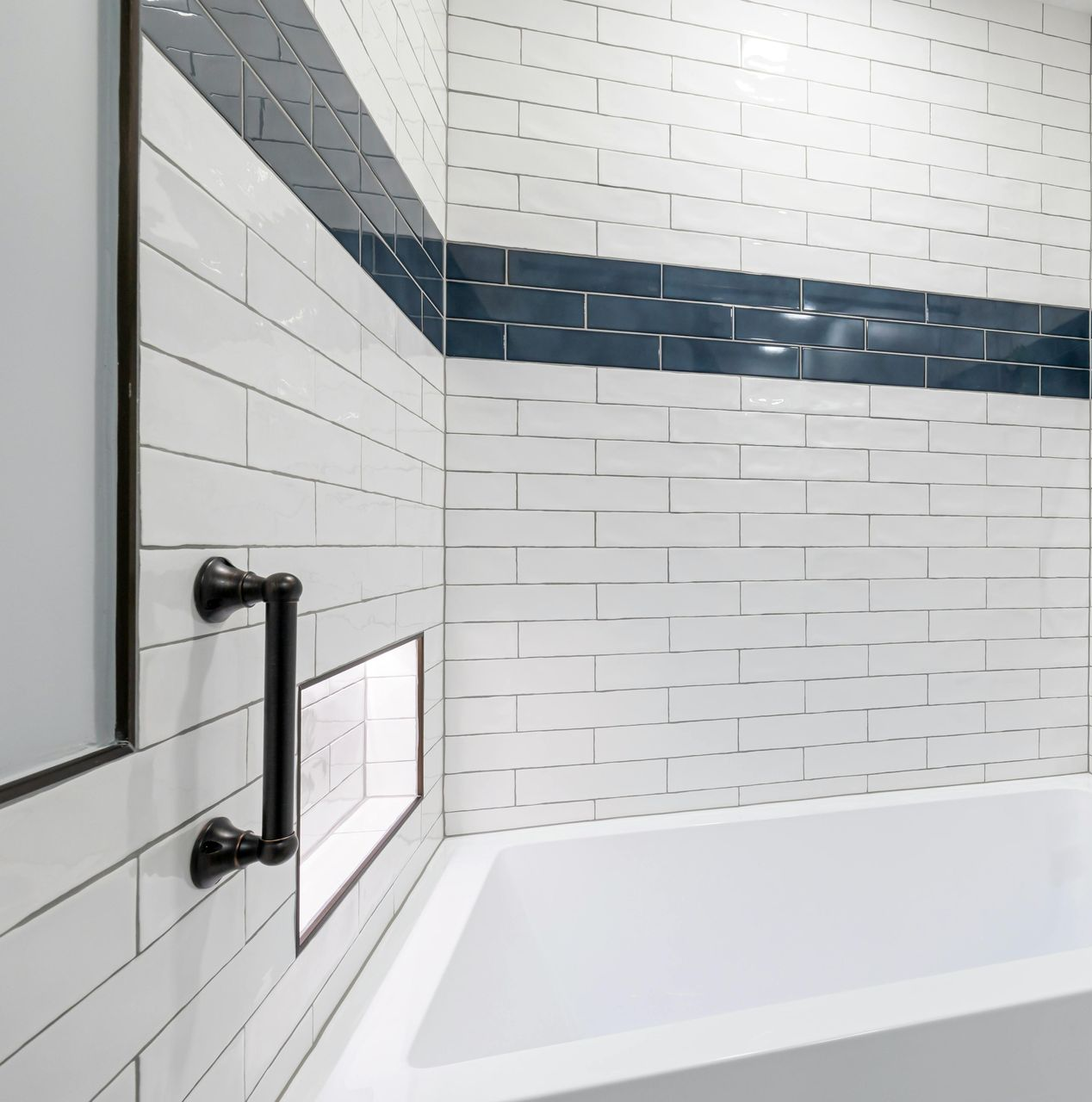 A white subway-tiled bathroom wall with a black accent tile stripe, a black grab bar, and a built-in recessed shelf.