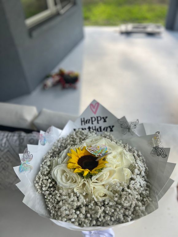 A bouquet of white roses and baby 's breath with a sunflower on top