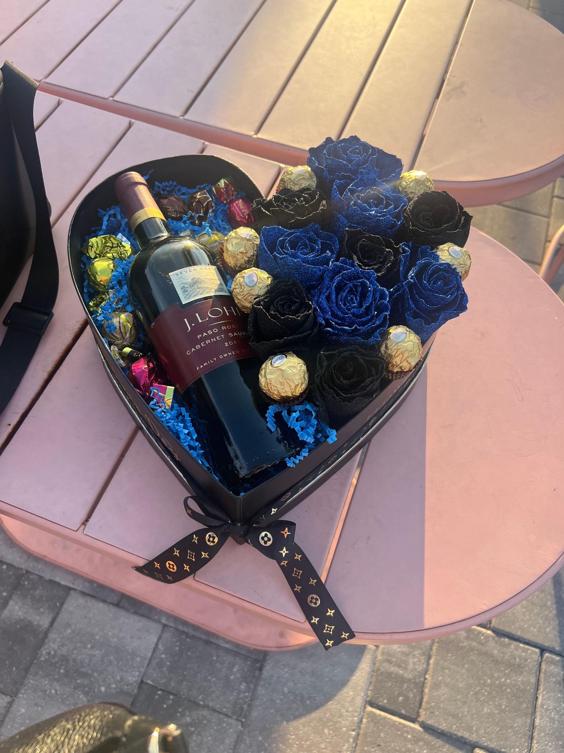 A heart shaped box filled with flowers and a bottle of wine