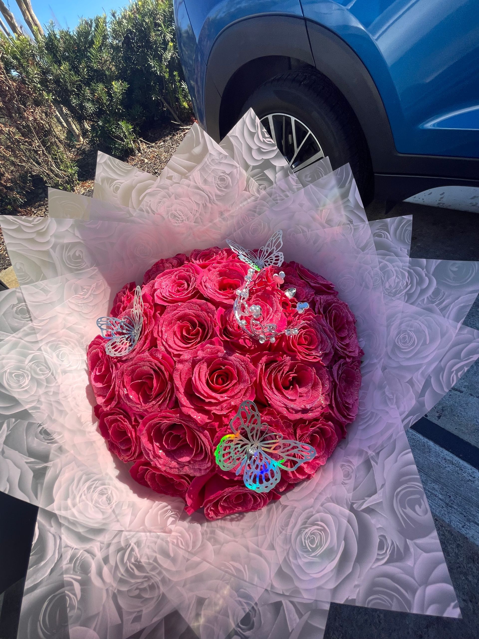 A bouquet of pink roses is sitting in front of a blue car.